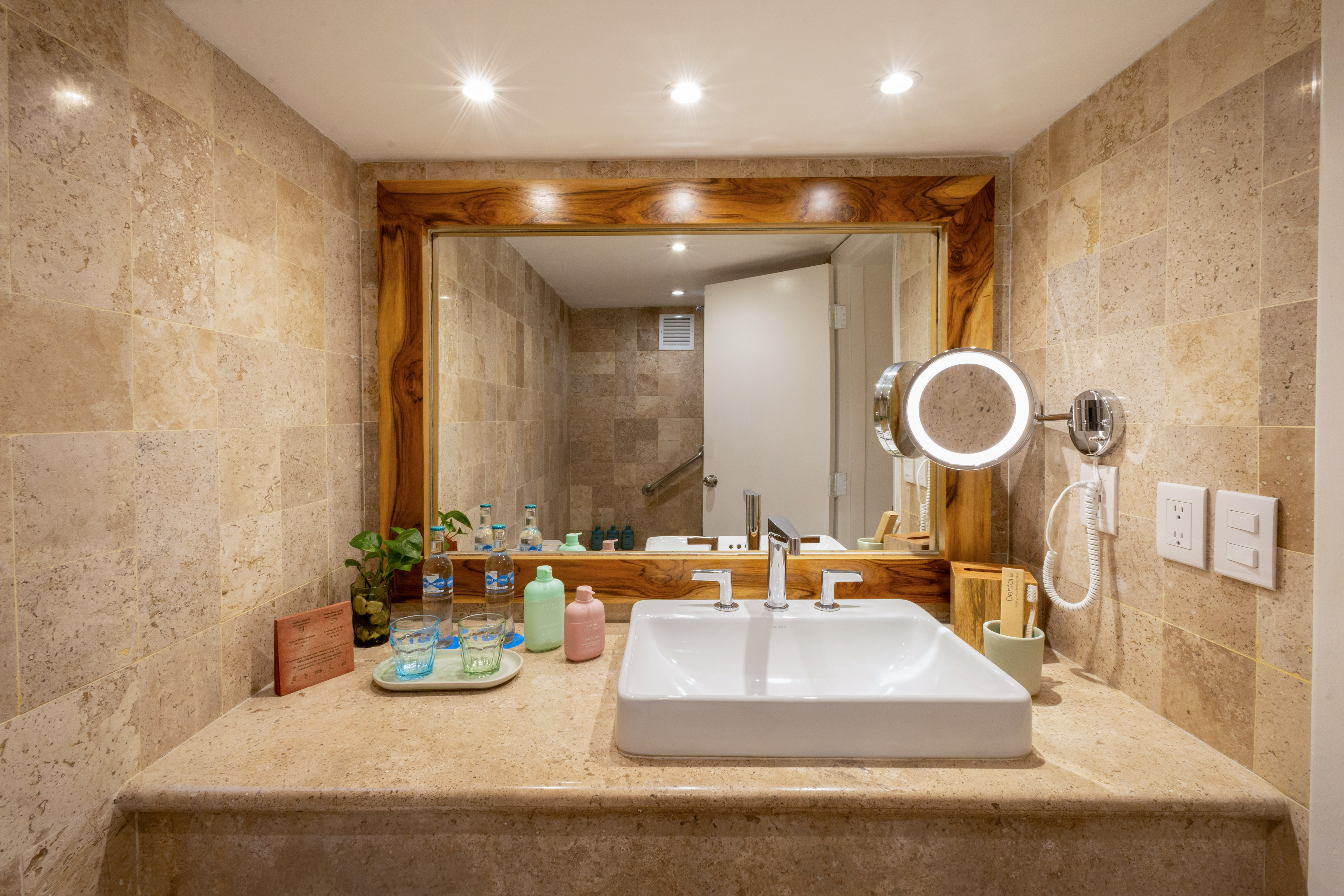 Luxury hotel bathroom with travertine vanity, sleek sink, and illuminated mirror.