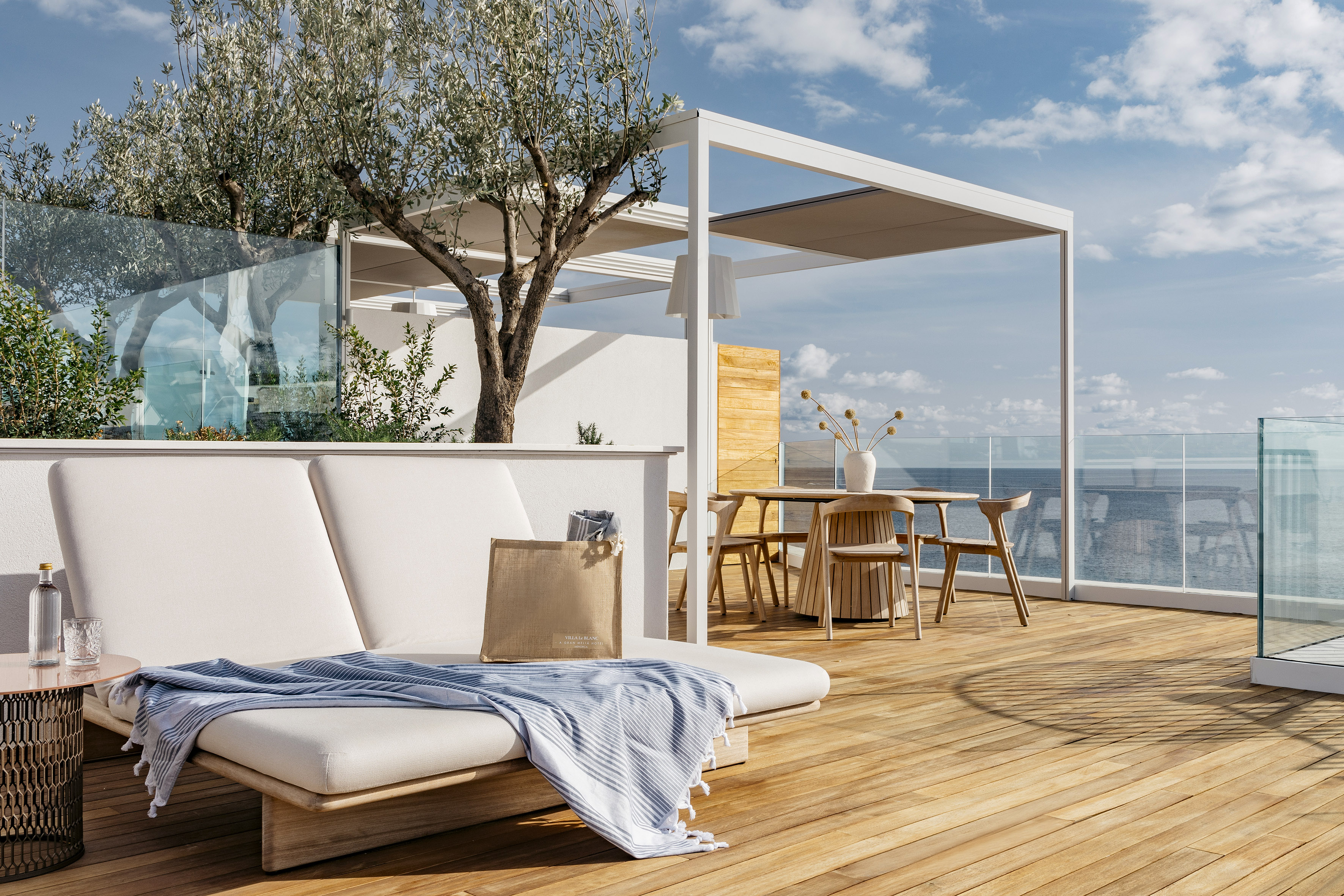 Oceanfront terrace with modern pergola, wooden deck, daybed, and dining area.