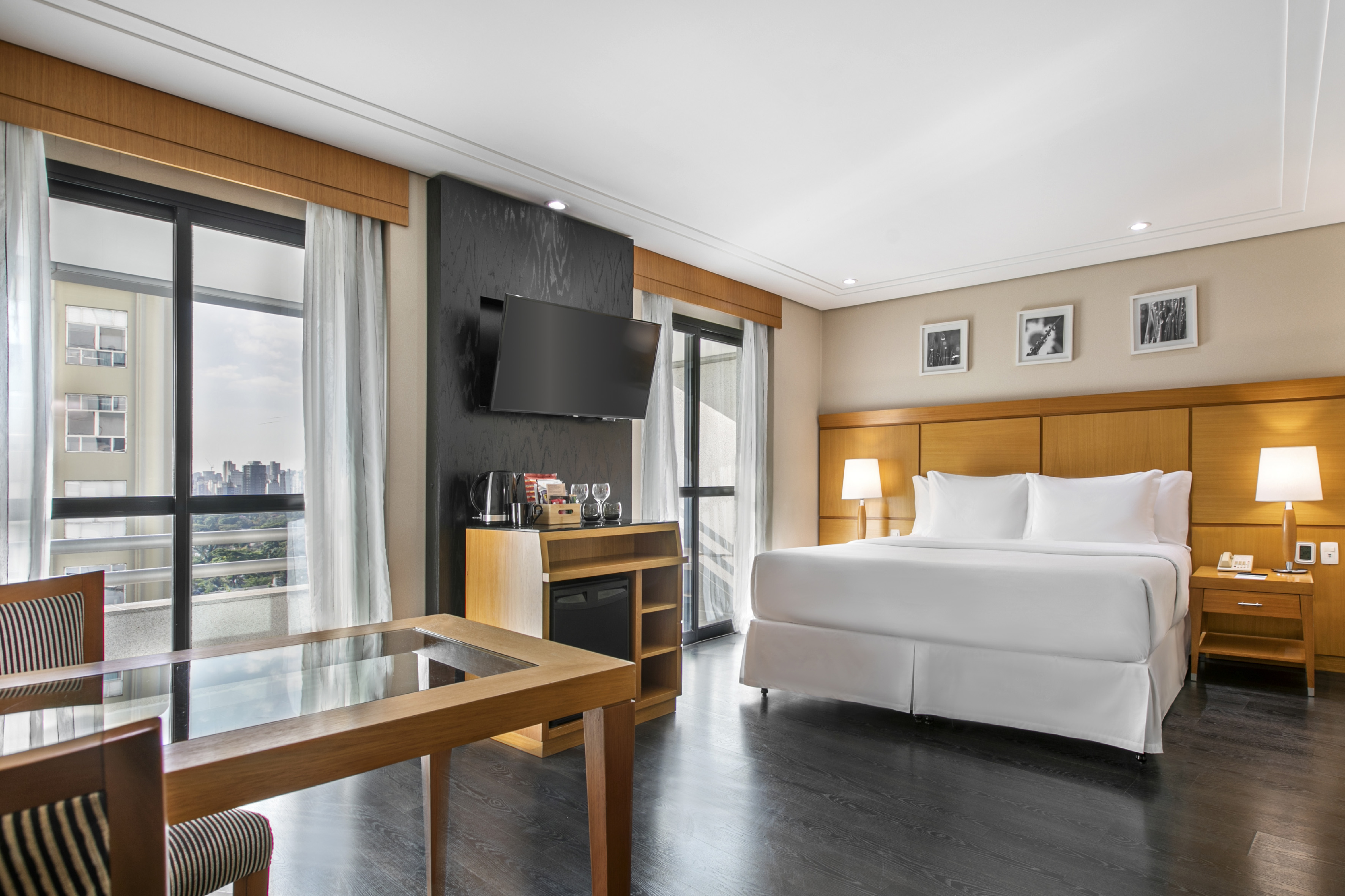 Modern hotel room with king bed, city view, wall TV, and work desk.
