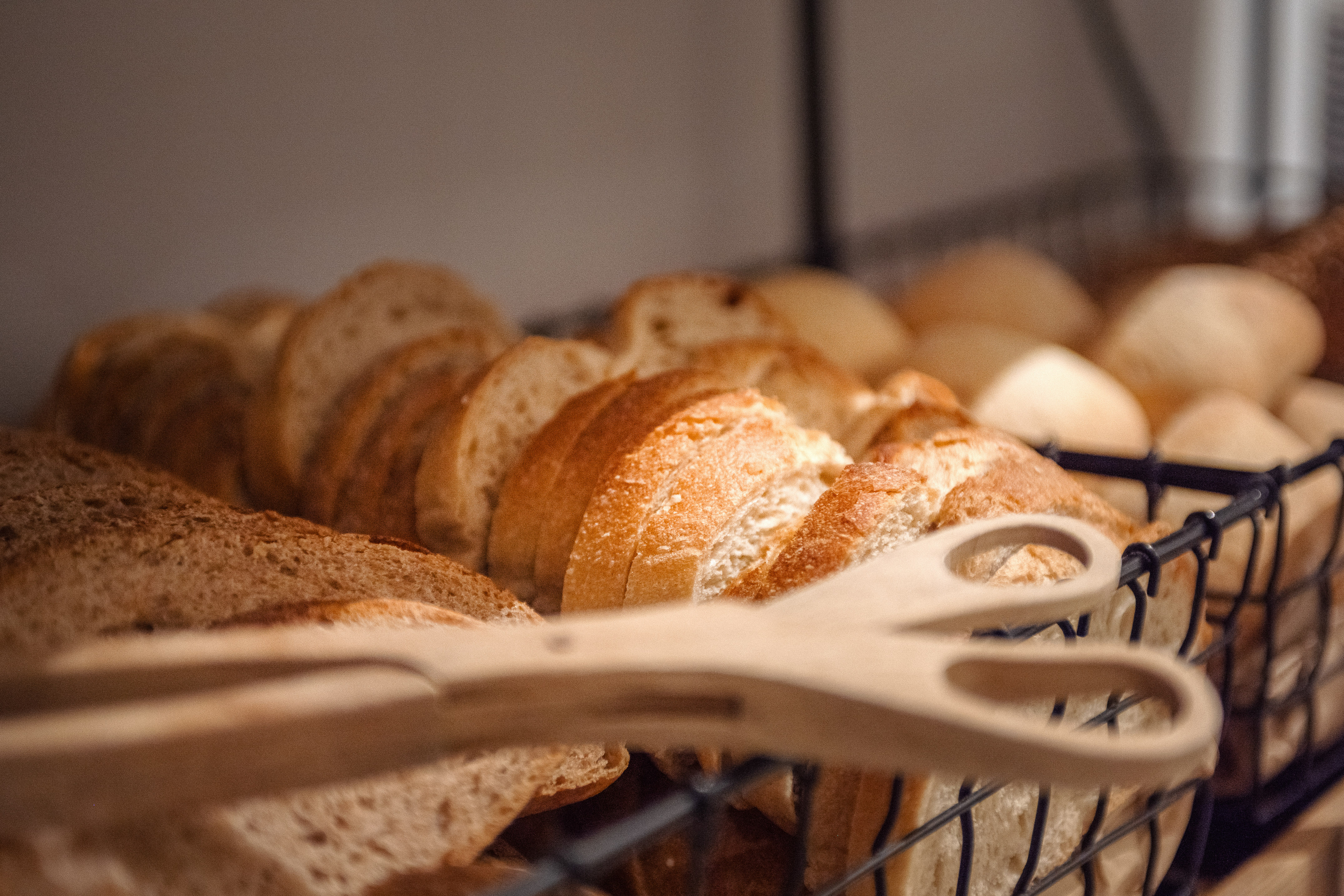 Fresh sliced bread and rolls in a basket with wooden tongs.