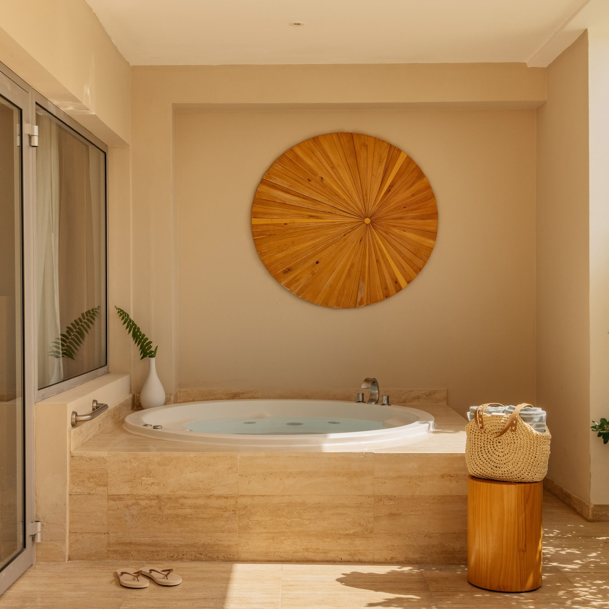 Outdoor hot tub on a sunny patio with wooden wall art and tropical plants.