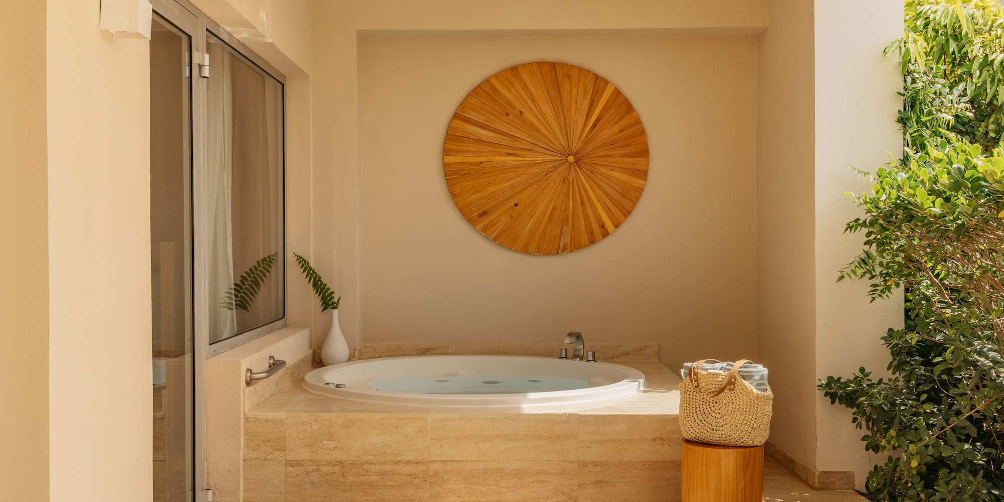 Outdoor hot tub on a sunny patio with wooden wall art and tropical plants.