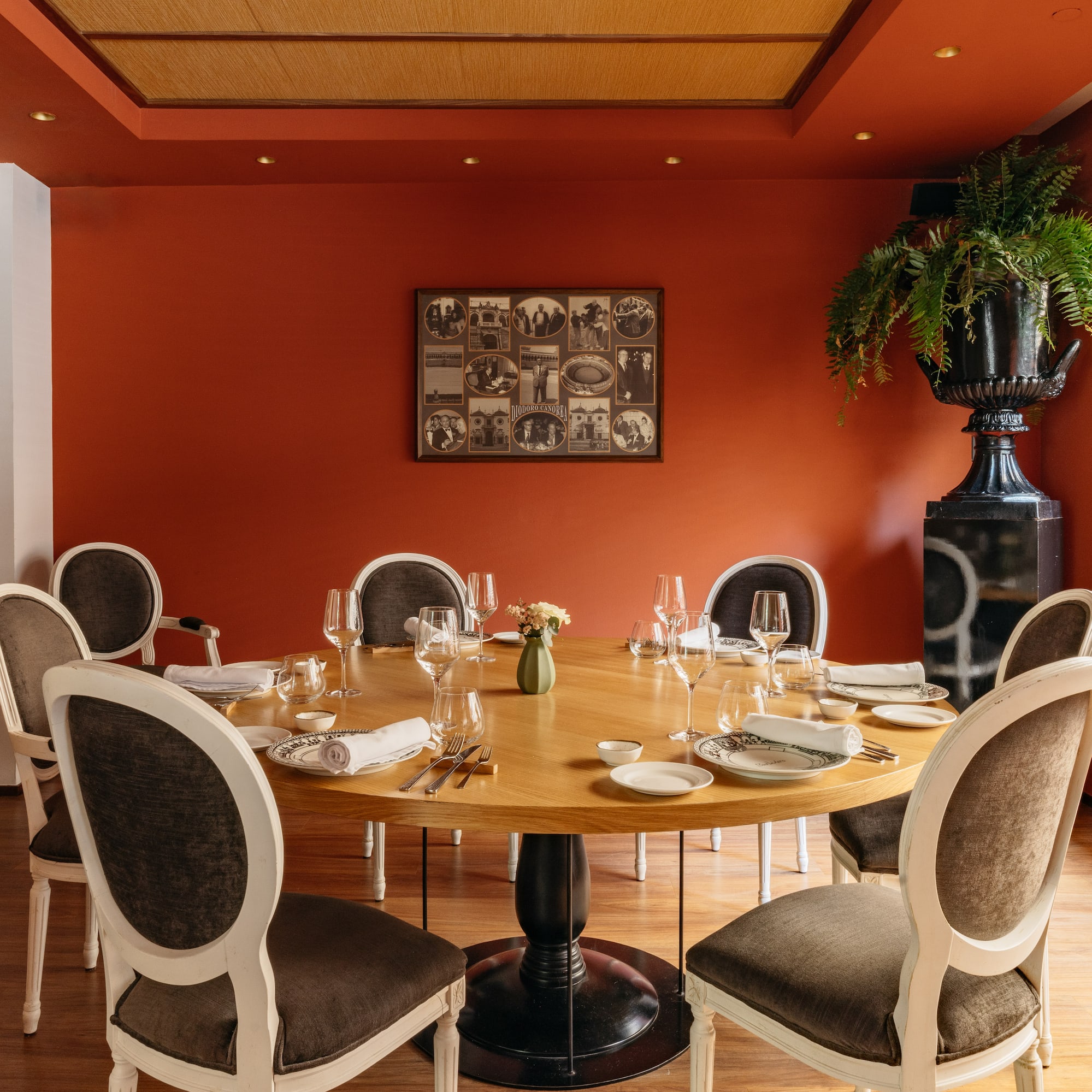 Restaurante elegante con mesa redonda, paredes terracota y sillas clásicas.