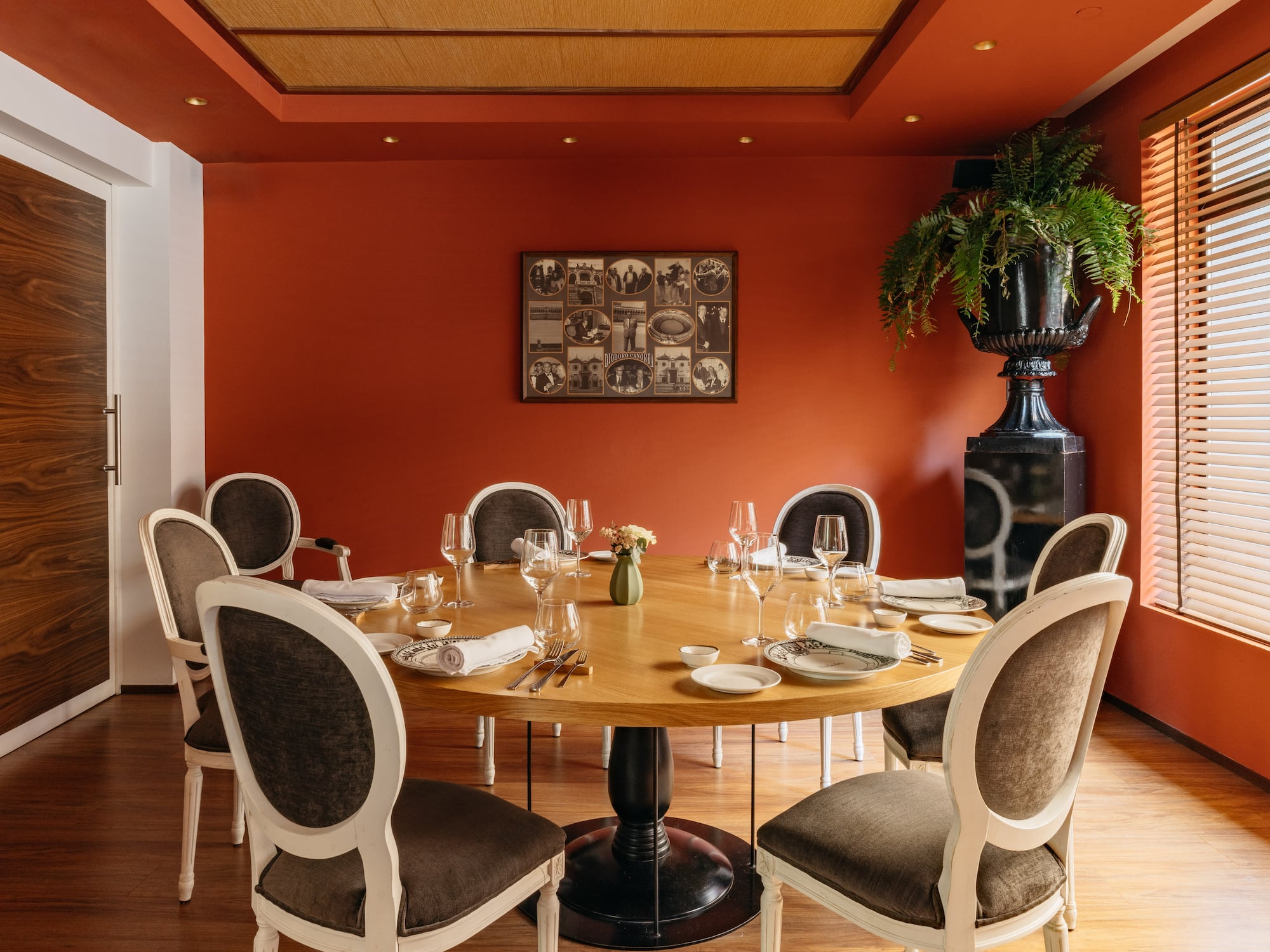 Restaurante elegante con mesa redonda, paredes terracota y sillas clásicas.