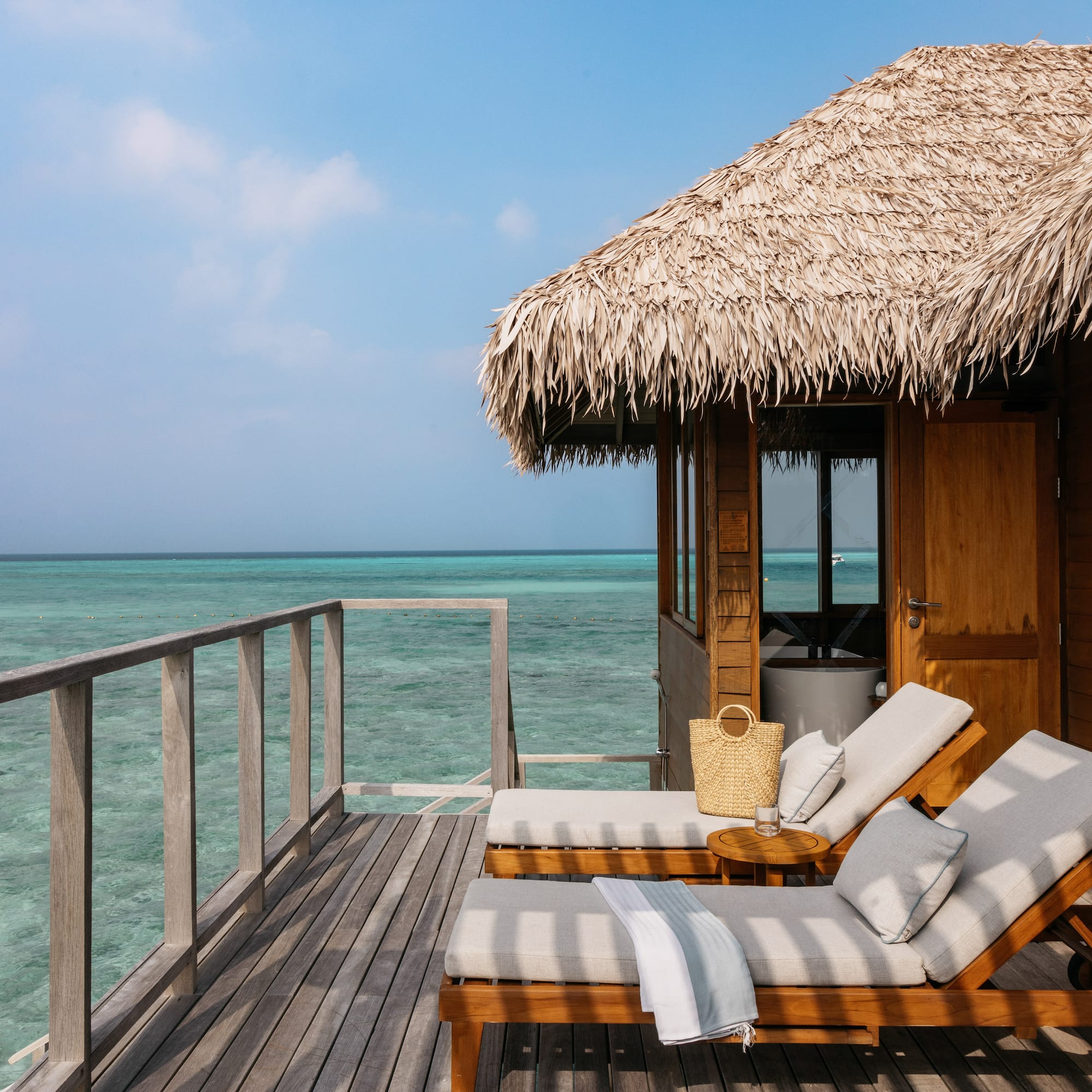 a deck with chairs and a straw roof on a beach