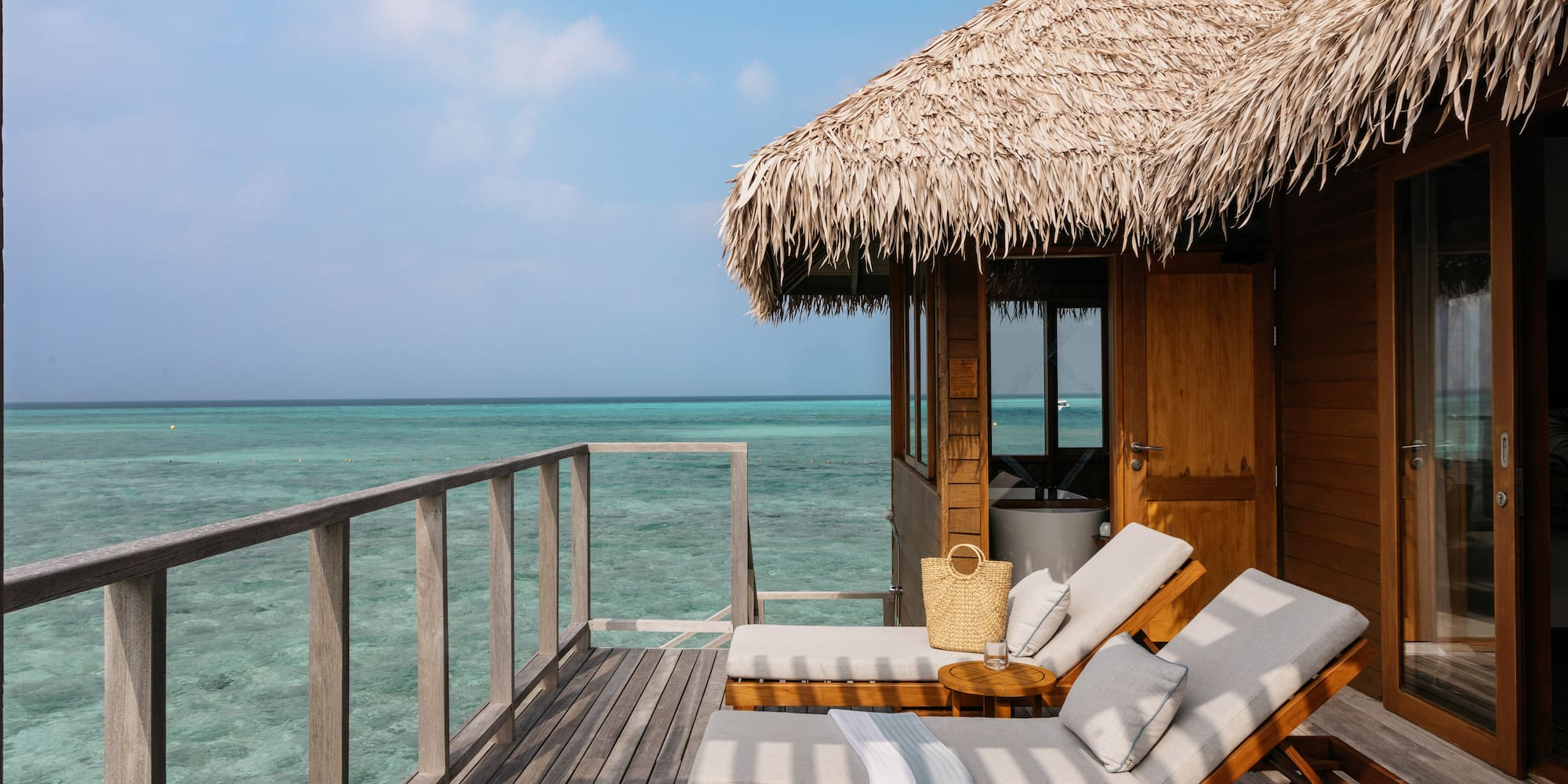 a deck with chairs and a straw roof on a beach