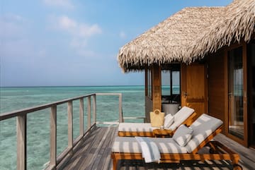 a deck with chairs and a straw roof on a beach
