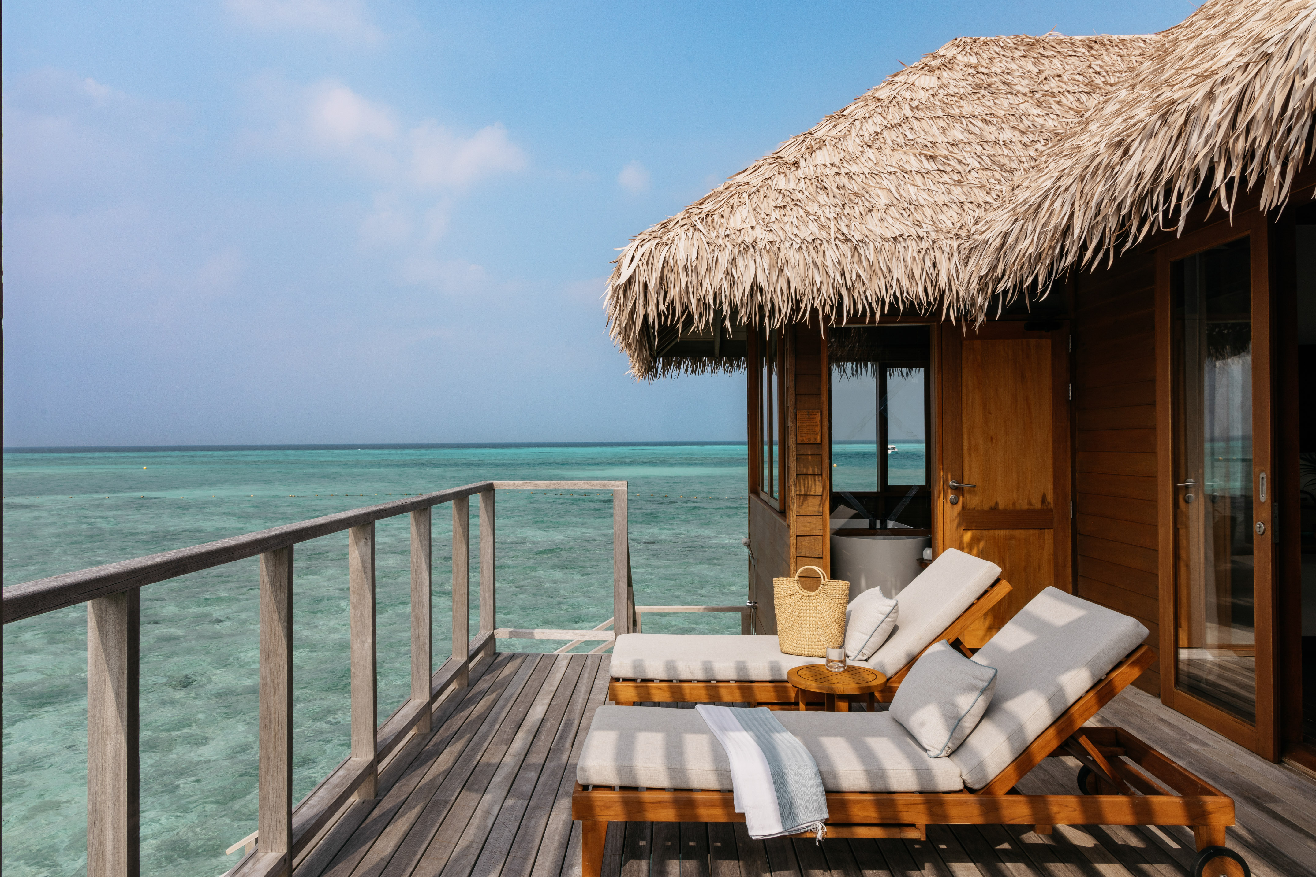 a deck with chairs and a straw roof on a beach