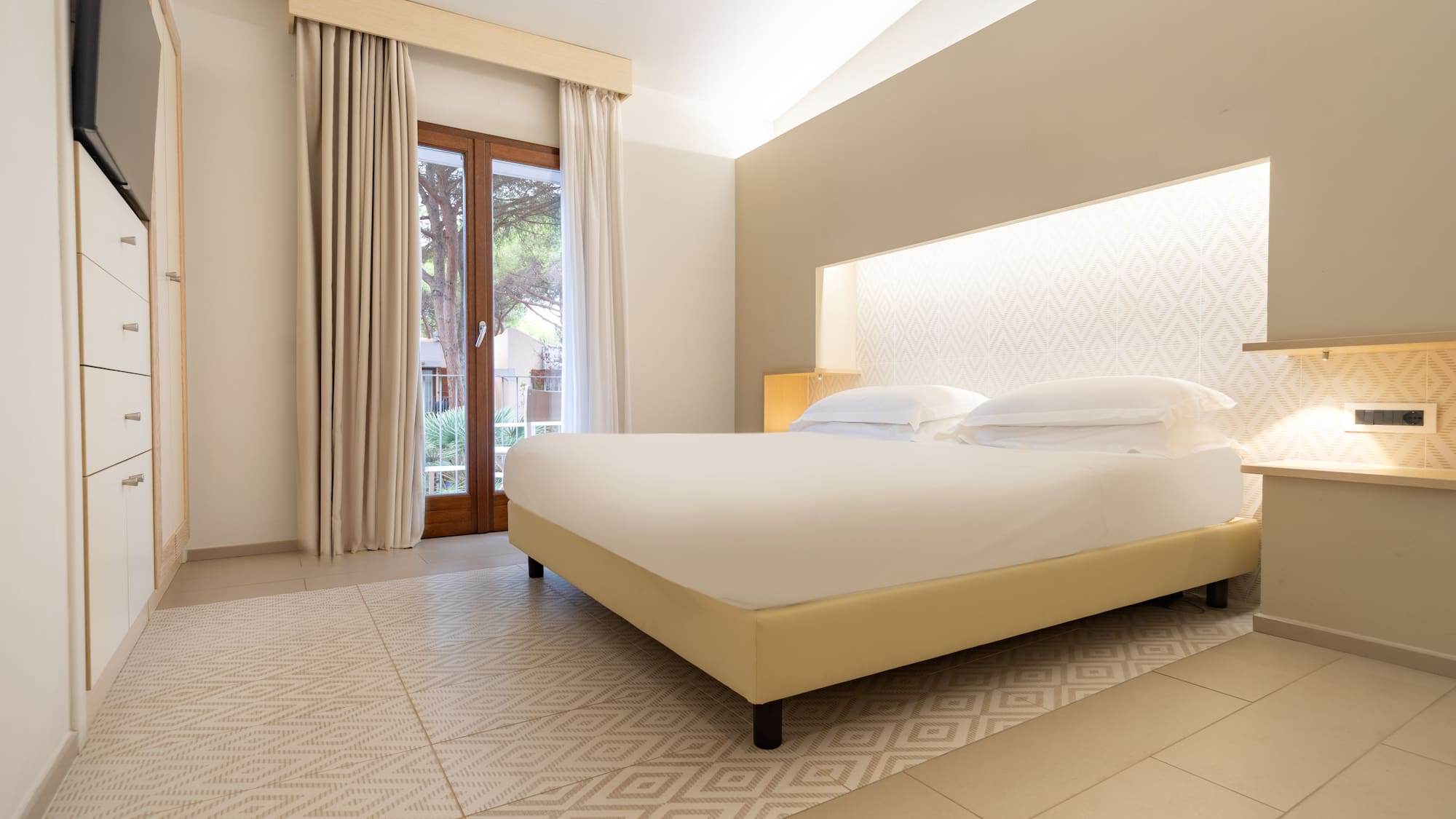 Bright modern hotel bedroom with king bed, patterned headboard, and balcony.