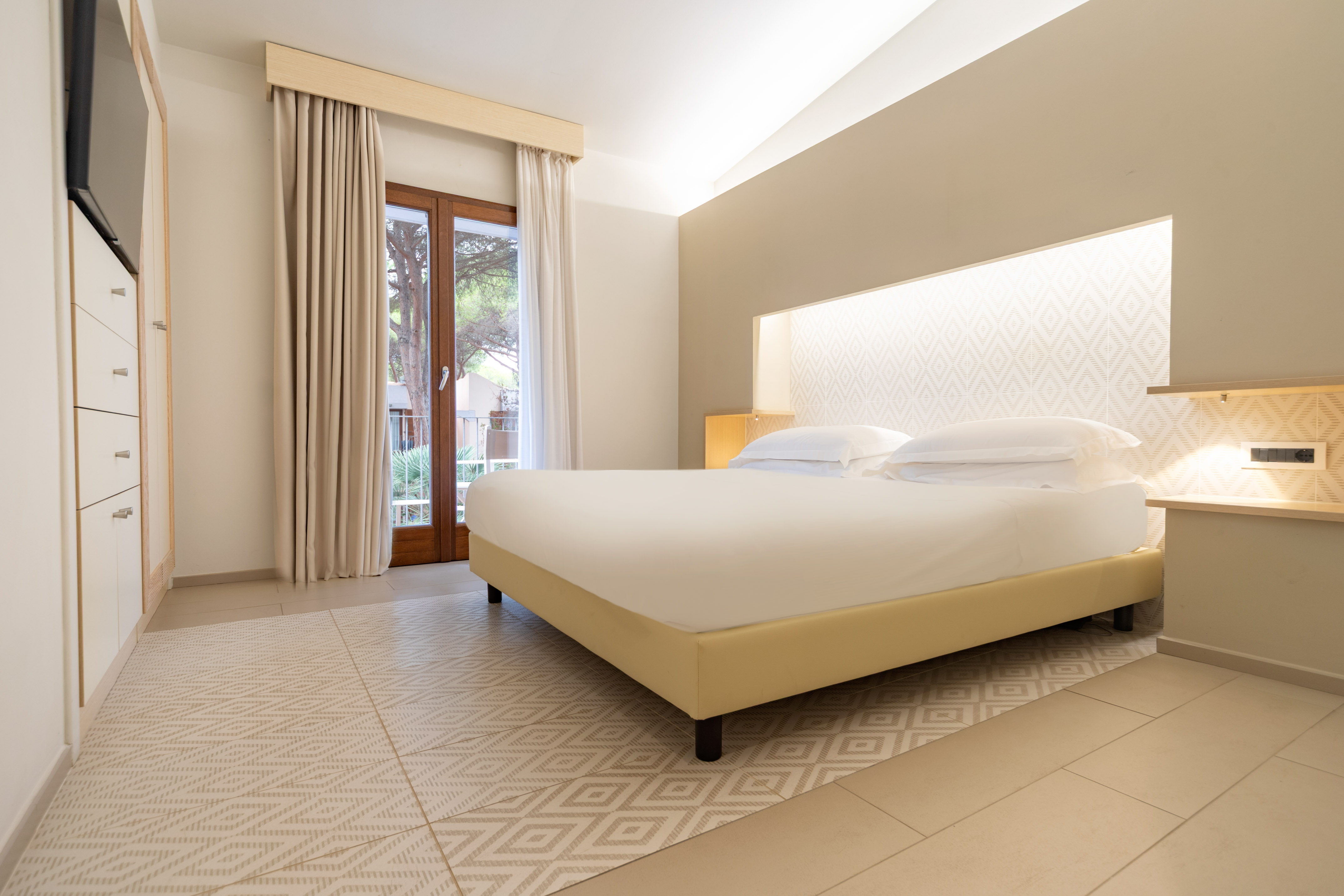 Bright modern hotel bedroom with king bed, patterned headboard, and balcony.