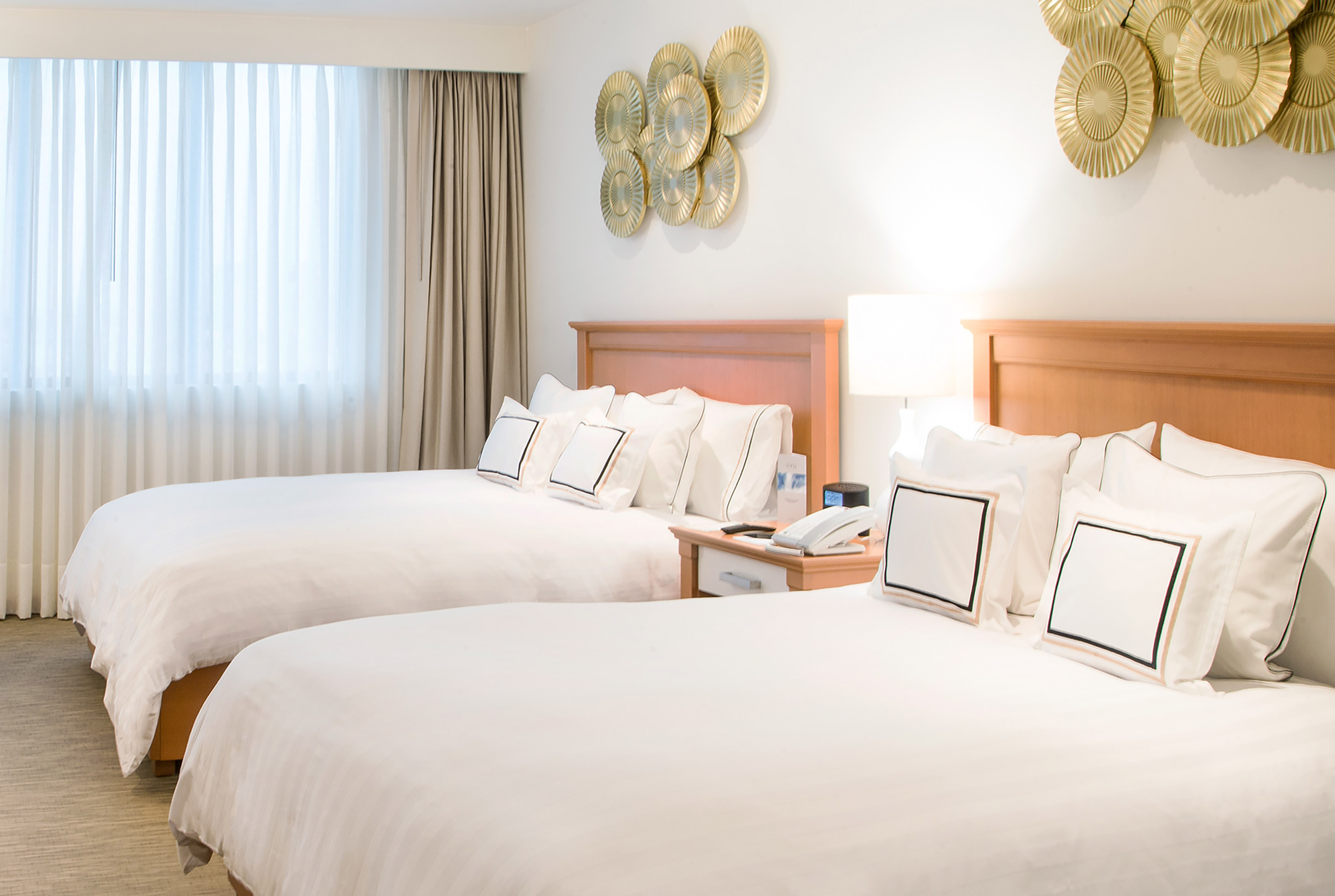 Two beds, white bedding, and modern gold wall decor in a bright hotel room.