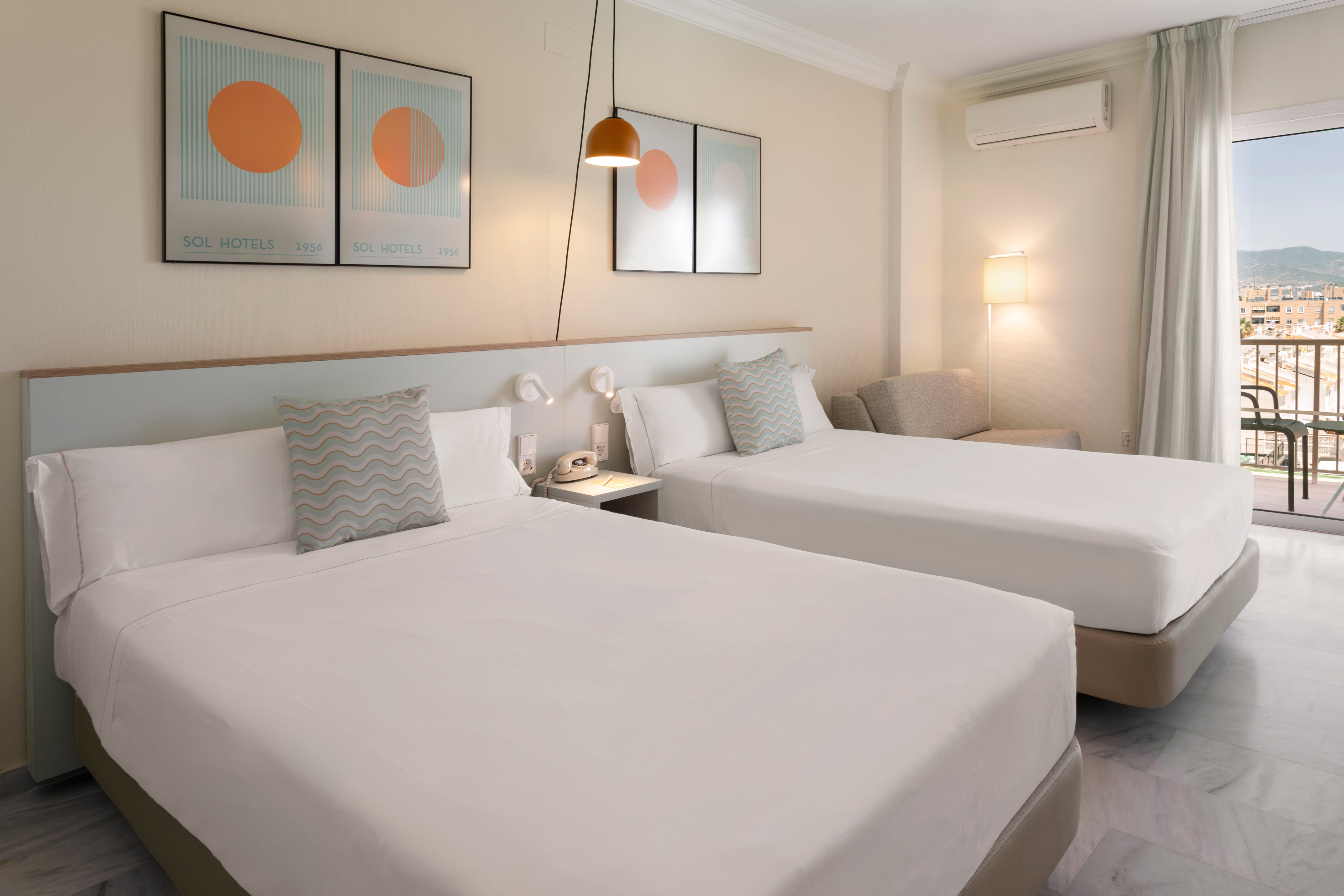 Bright hotel room with twin beds, balcony, city view, and modern furnishings.