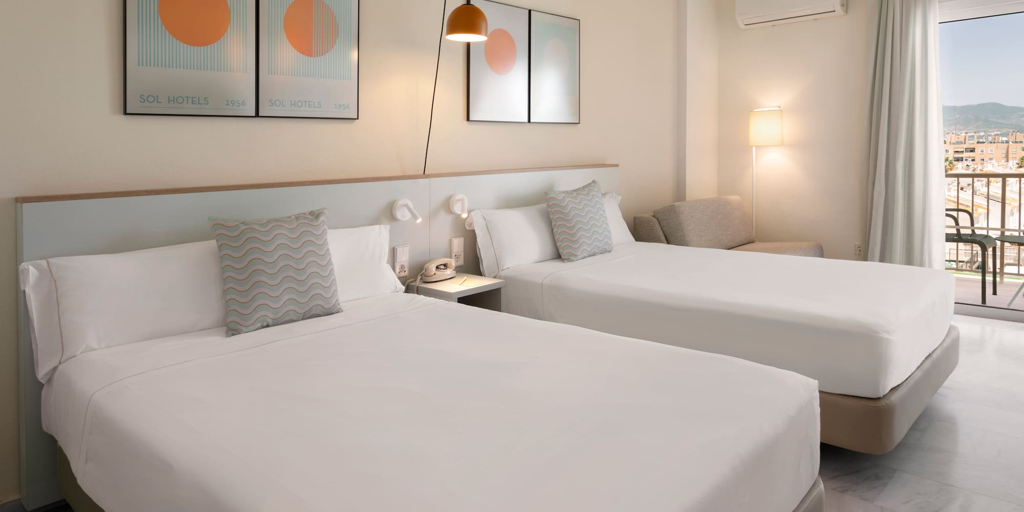 Bright hotel room with twin beds, balcony, city view, and modern furnishings.