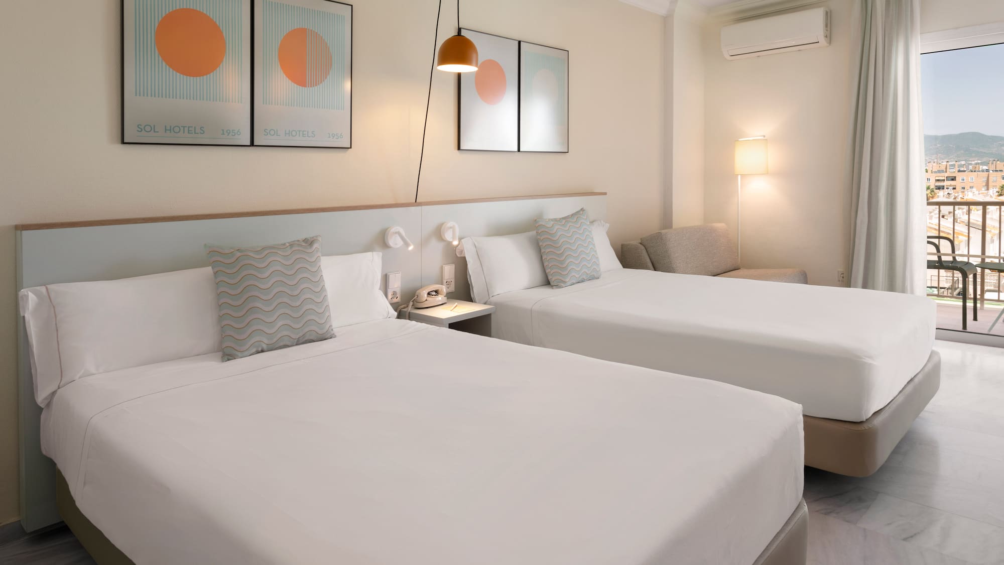 Bright hotel room with twin beds, balcony, city view, and modern furnishings.