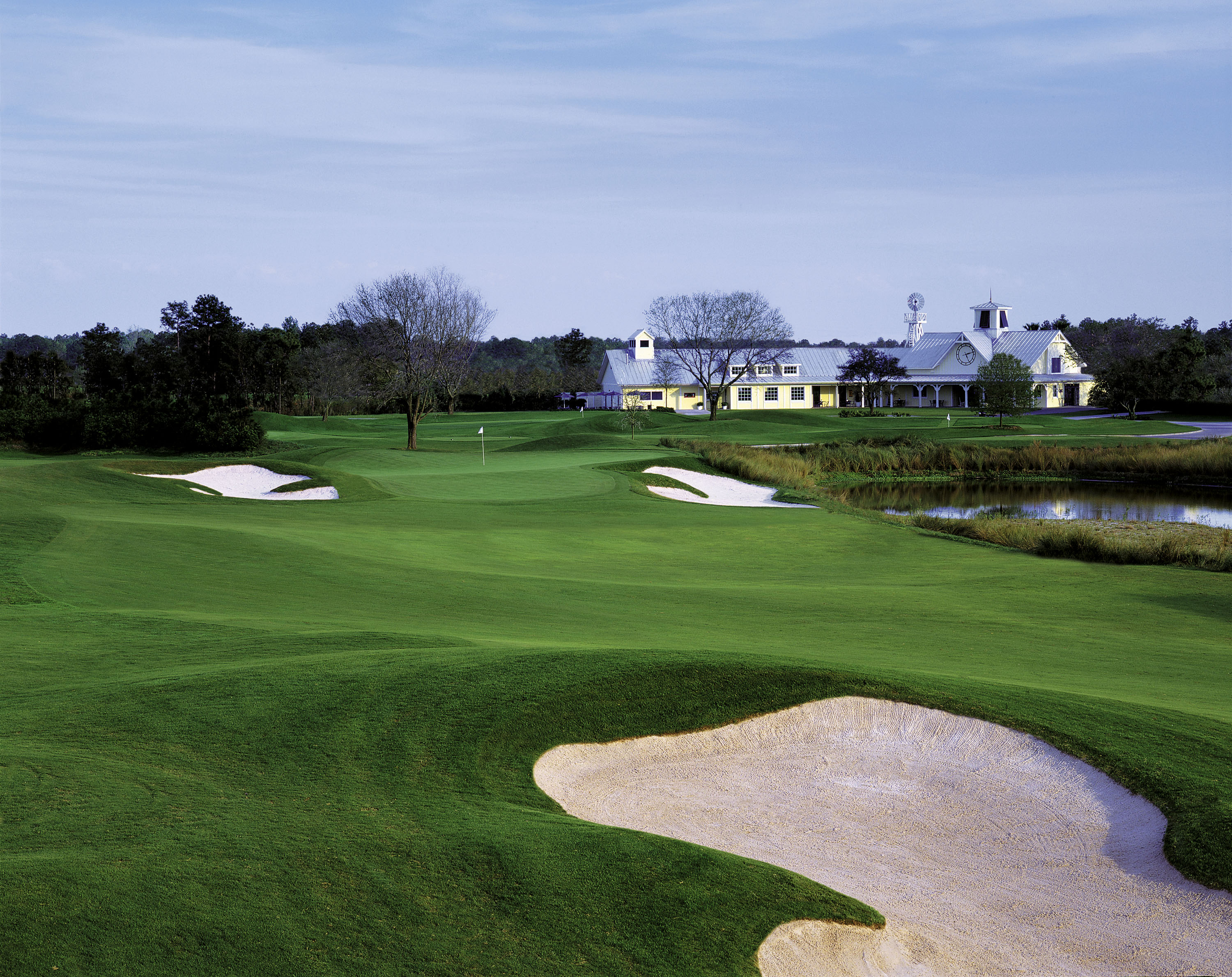 Lush golf course with sand traps, pond, and white clubhouse building.