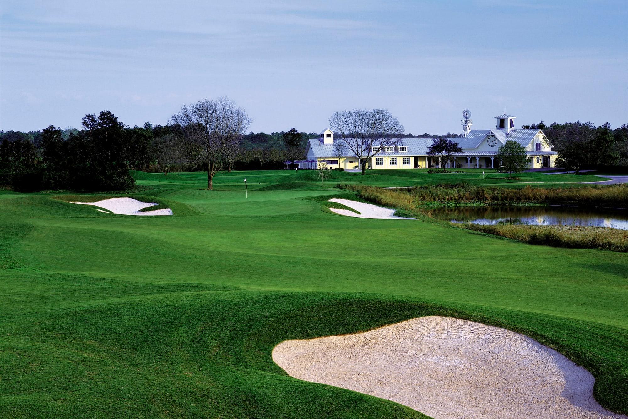 Lush golf course with sand traps, pond, and white clubhouse building.