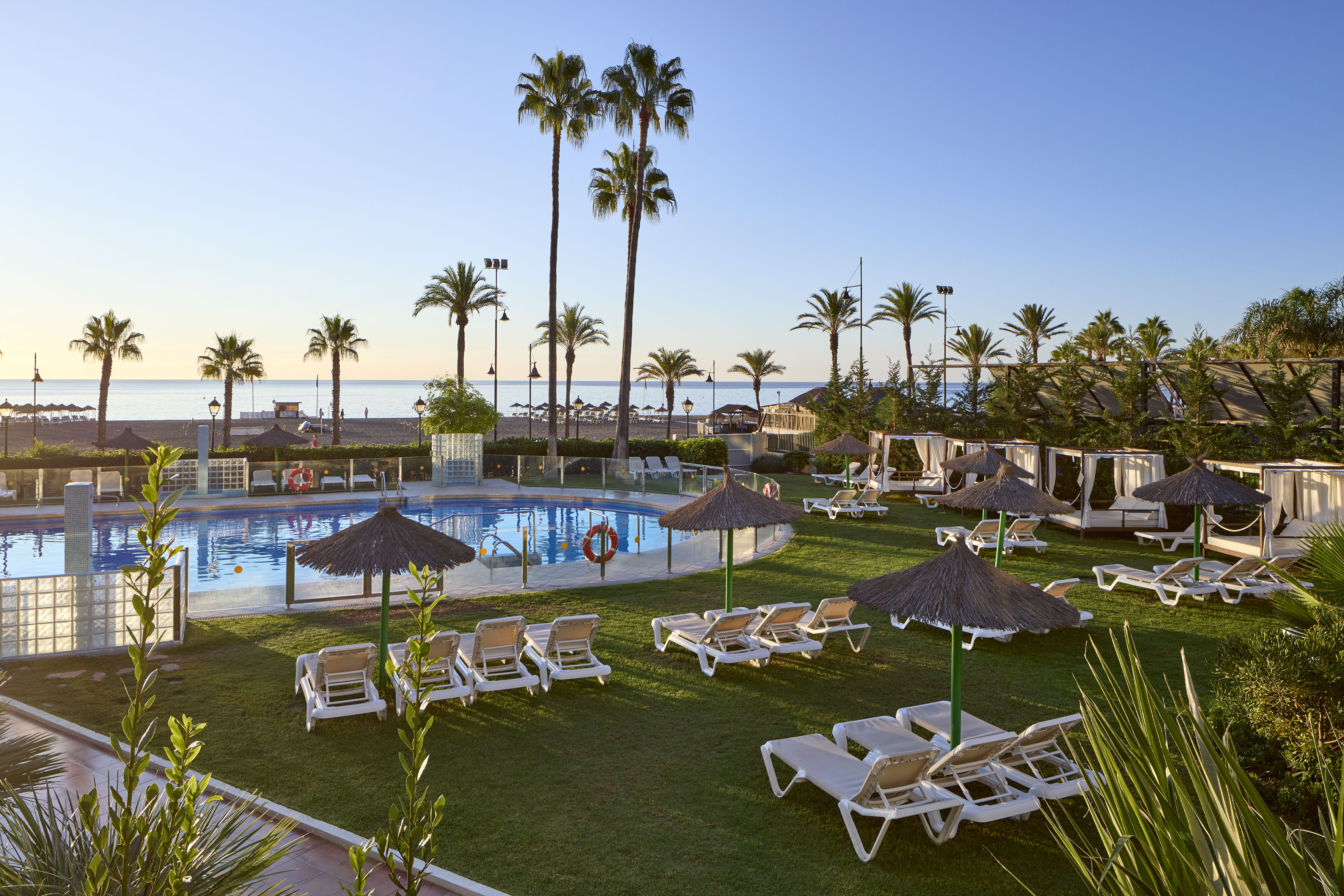 Resort pool with palm trees, beach, ocean view, sunbeds, and cabanas.