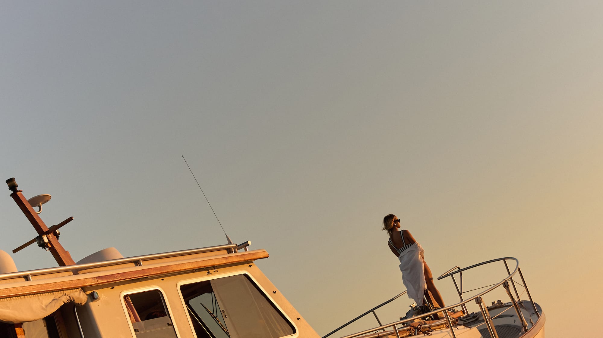 Atardecer dorado sobre mujer de pie en la proa de un barco en el mar.