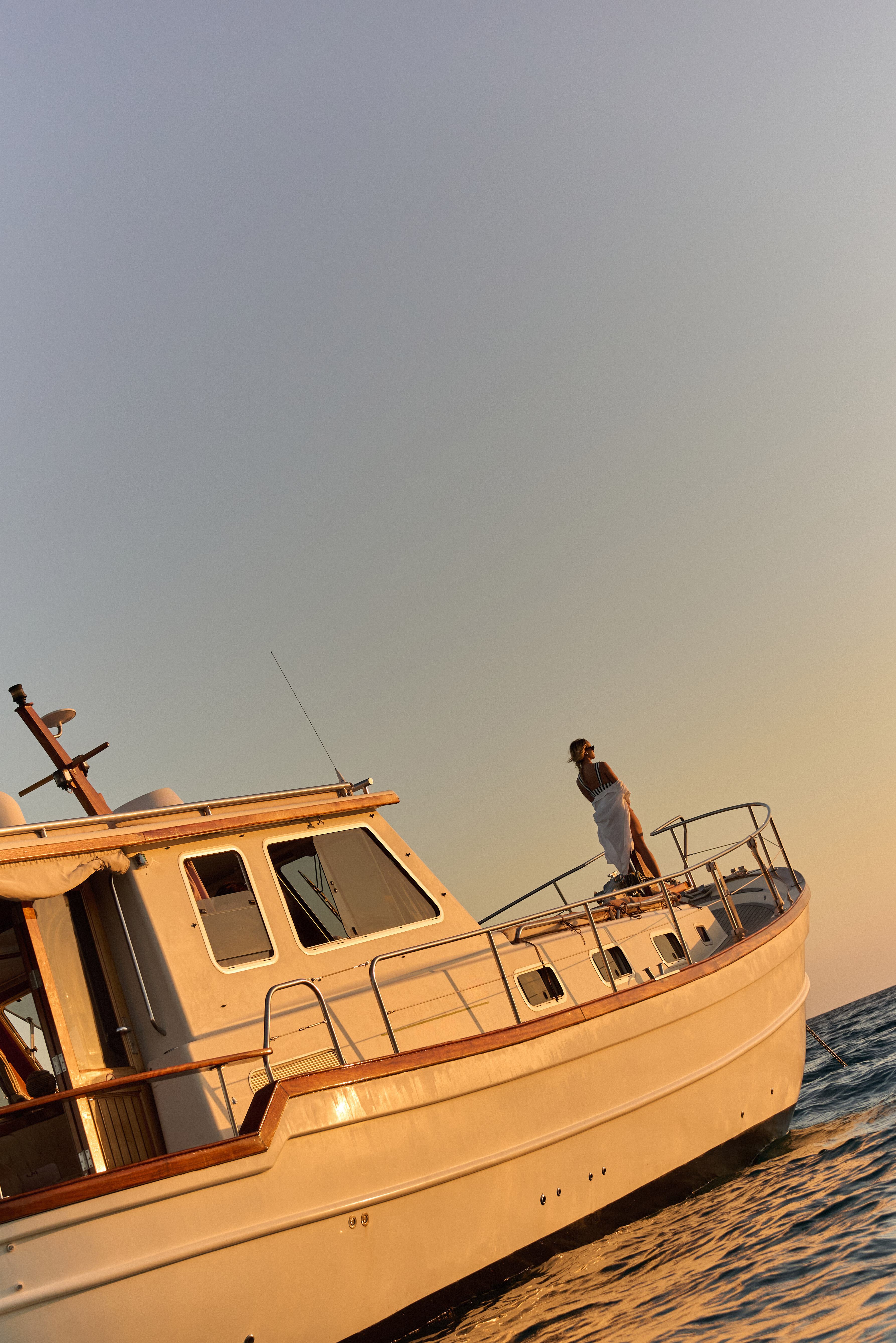 Atardecer dorado sobre mujer de pie en la proa de un barco en el mar.