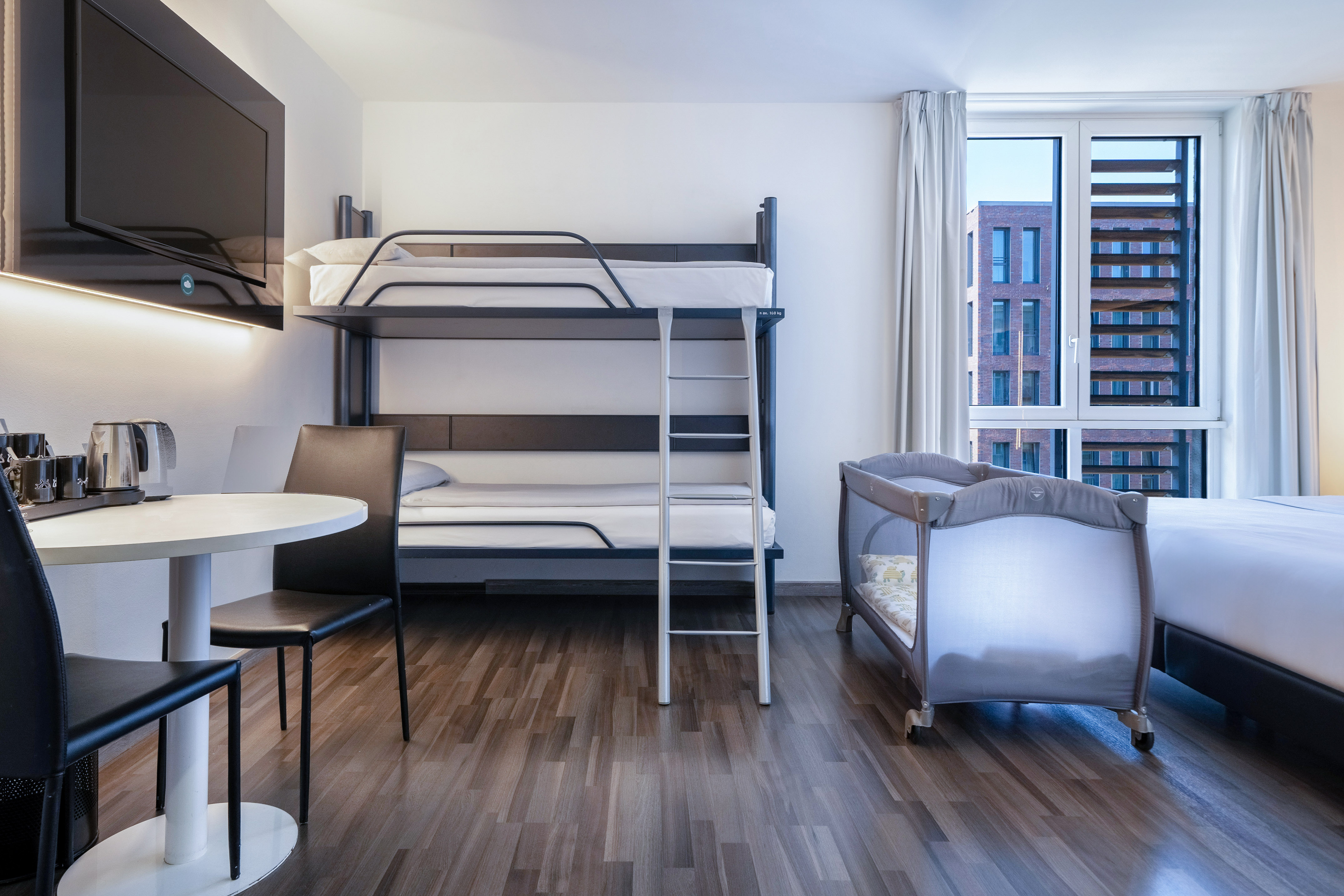 Modern family hotel room with bunk beds, TV, dining table, and baby crib.