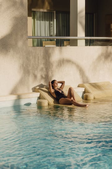 a woman in a swimsuit sitting on a lounger by a pool