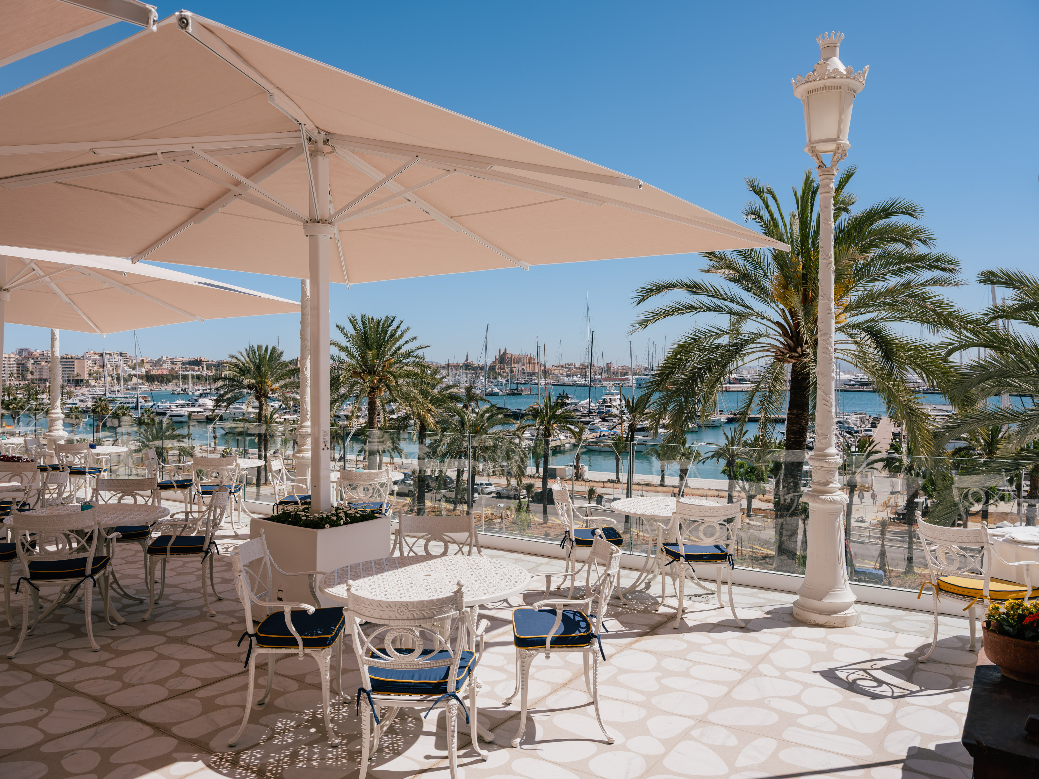 Waterfront patio with white tables, umbrellas, blue chairs, and marina view.