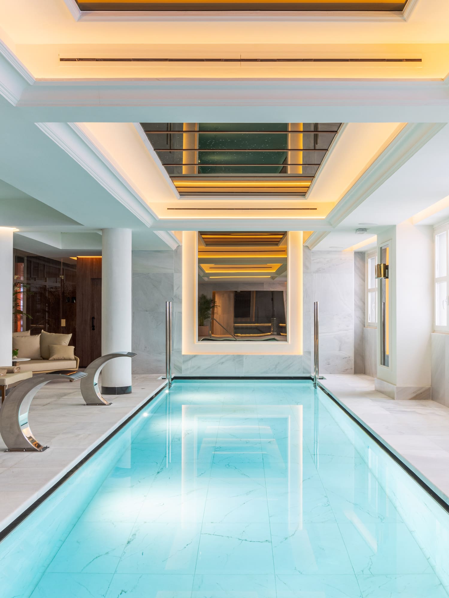 Luxury indoor swimming pool with marble, warm lighting, and lounge chairs.