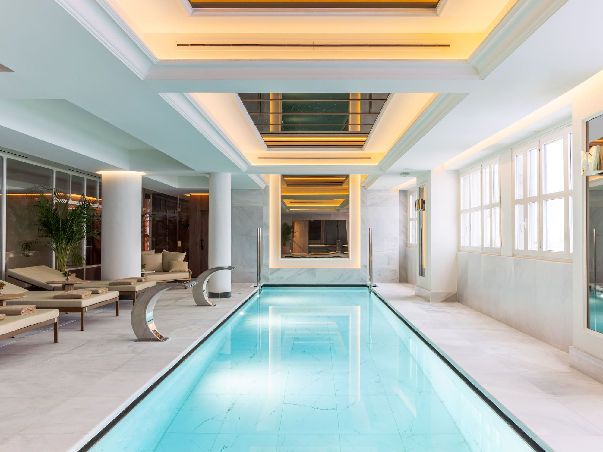 Elegant indoor pool with marble, lounge chairs, and warm lighting.