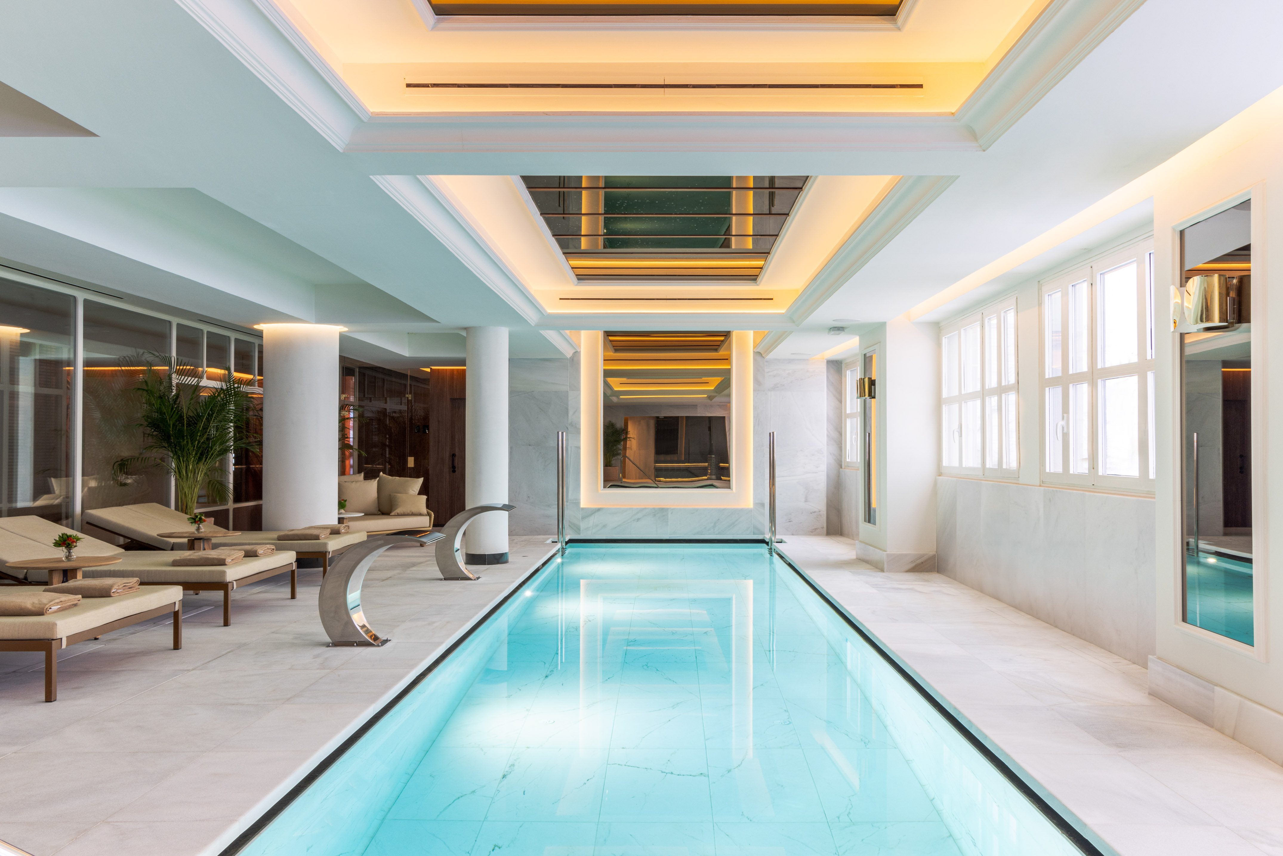 Luxury indoor swimming pool with marble, warm lighting, and lounge chairs.
