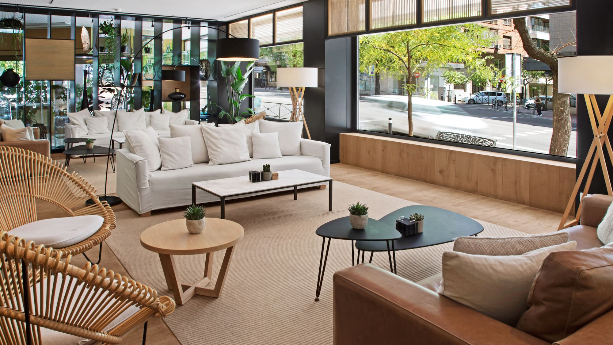 Bright, modern hotel lounge with white sofas, rattan chairs, and urban view.