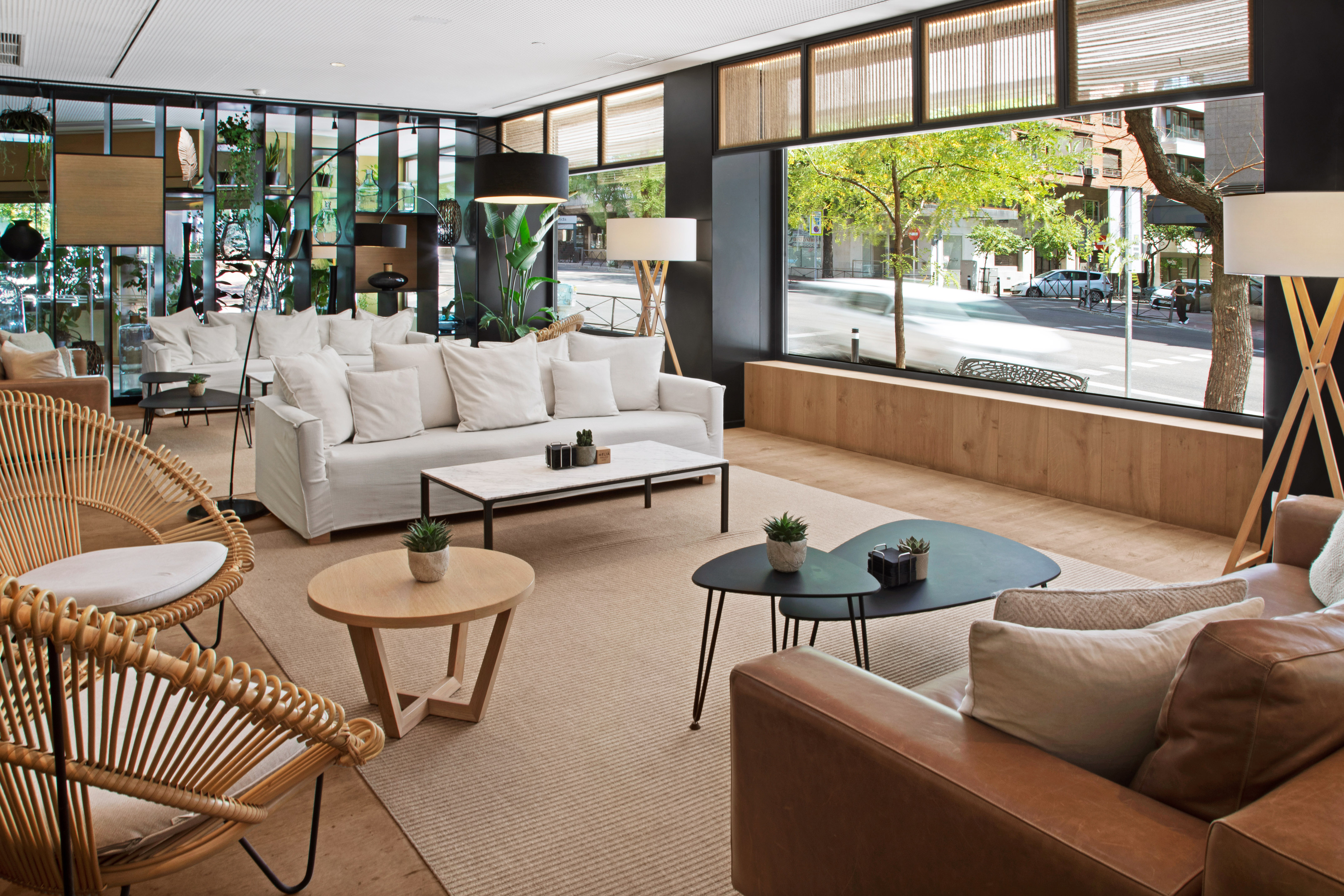 Modern hotel lobby with white sofas, rattan chairs, and city street view.