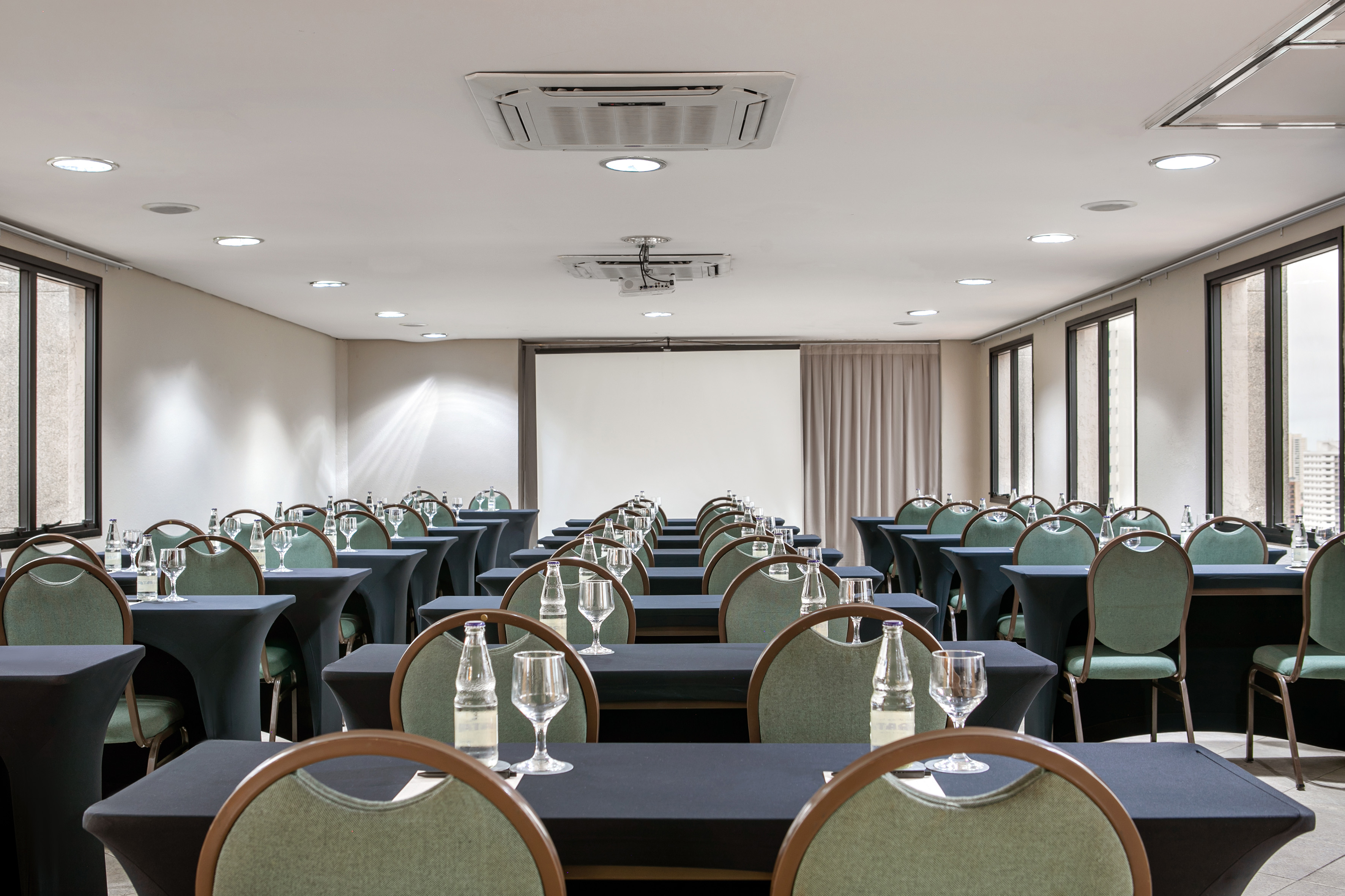 Conference room with classroom setup, projector screen, and green chairs.