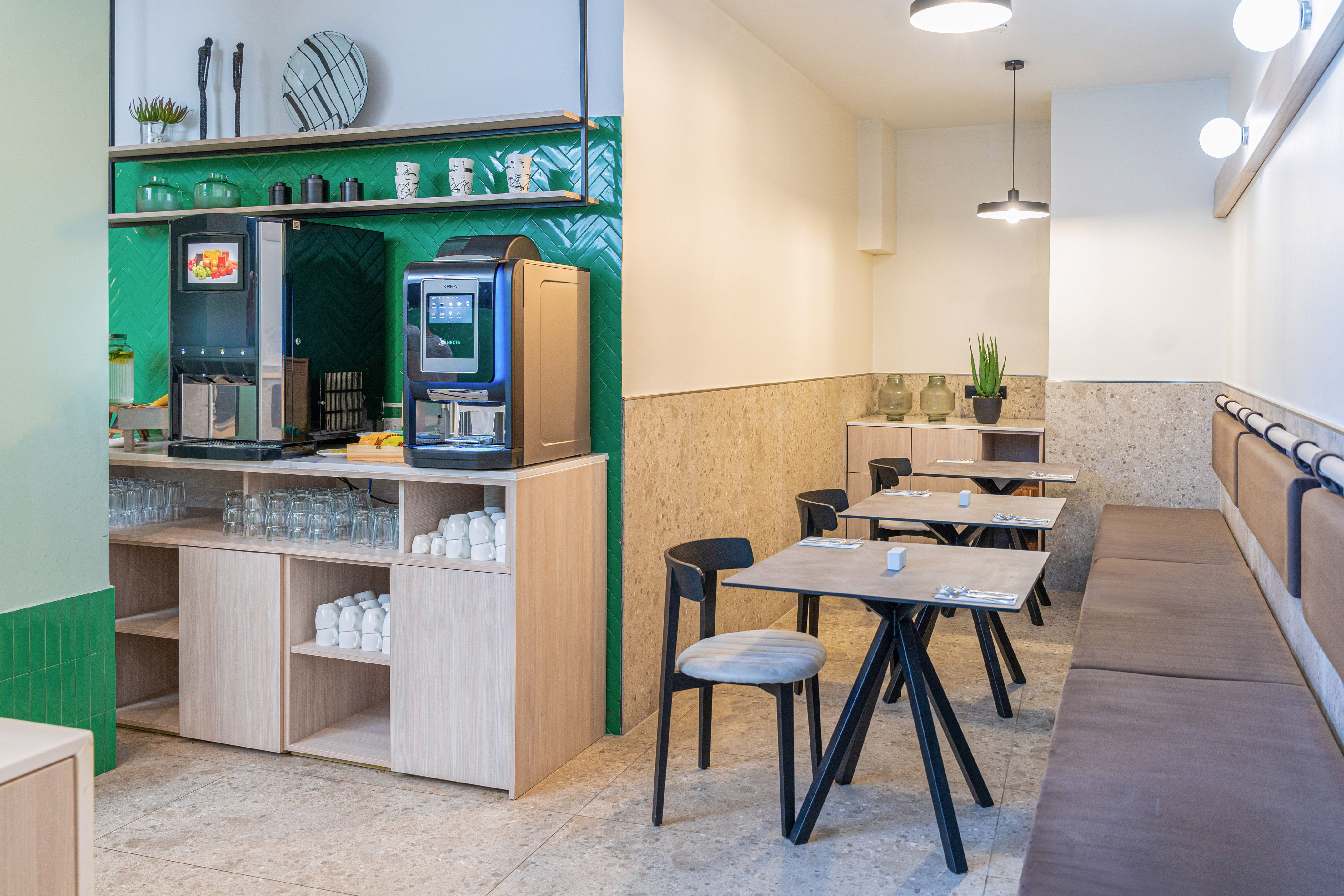 Modern self-service breakfast area with coffee and juice machines, tables.