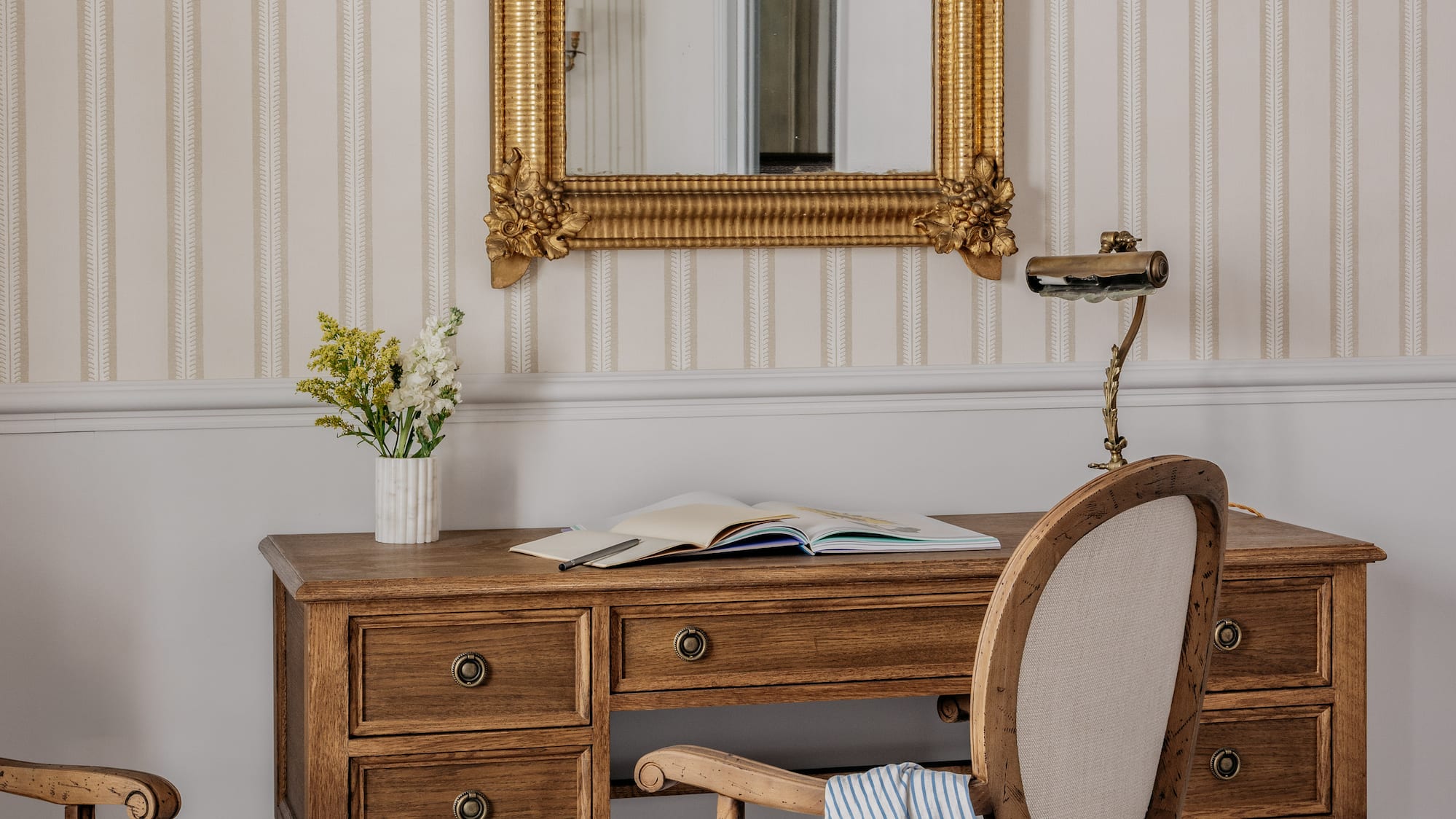 Classic wooden desk, gold mirror, striped wallpaper, checkered floor.