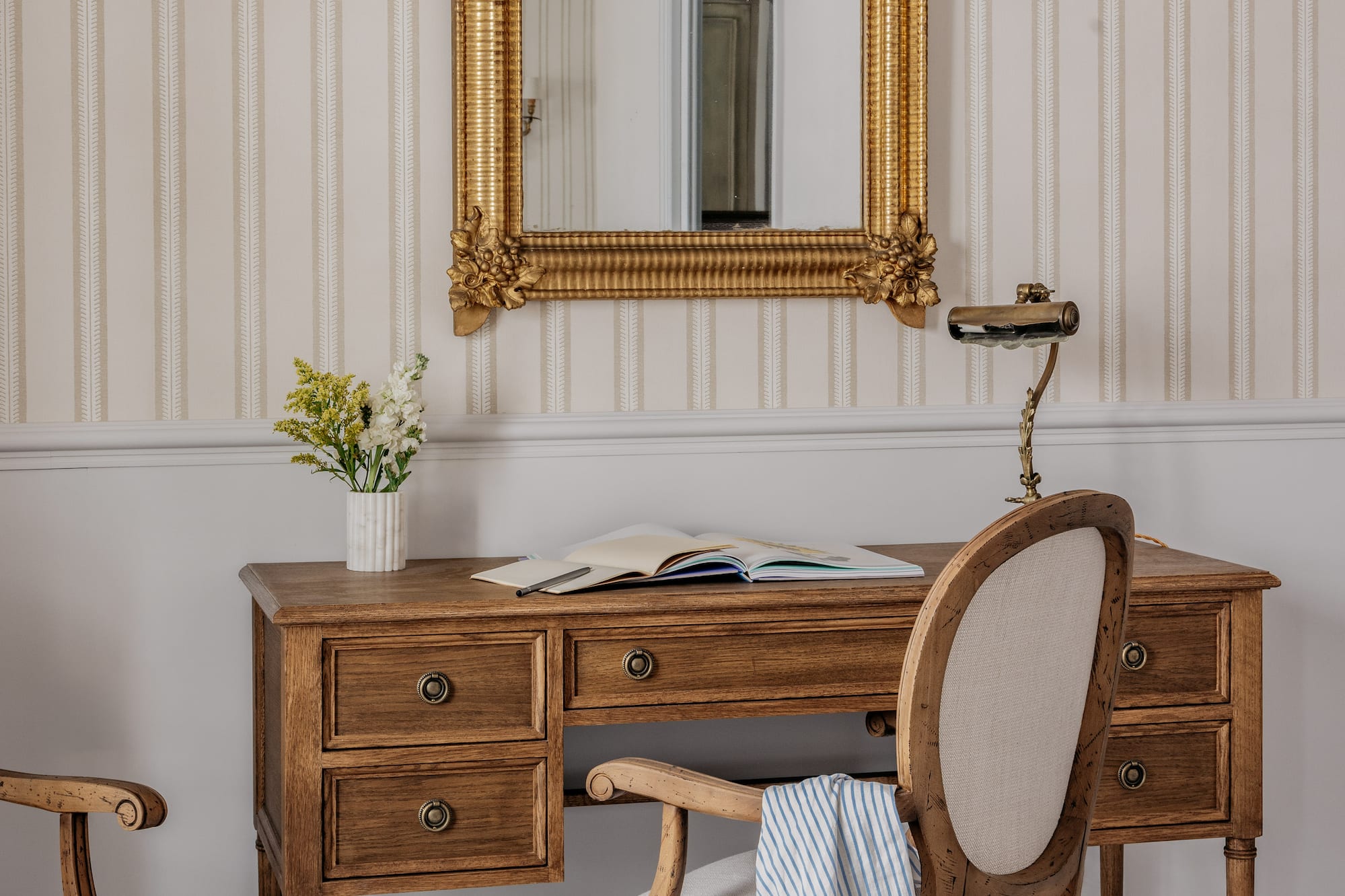 Estudio clásico con escritorio de madera, espejo dorado ornamentado y silla tapizada.