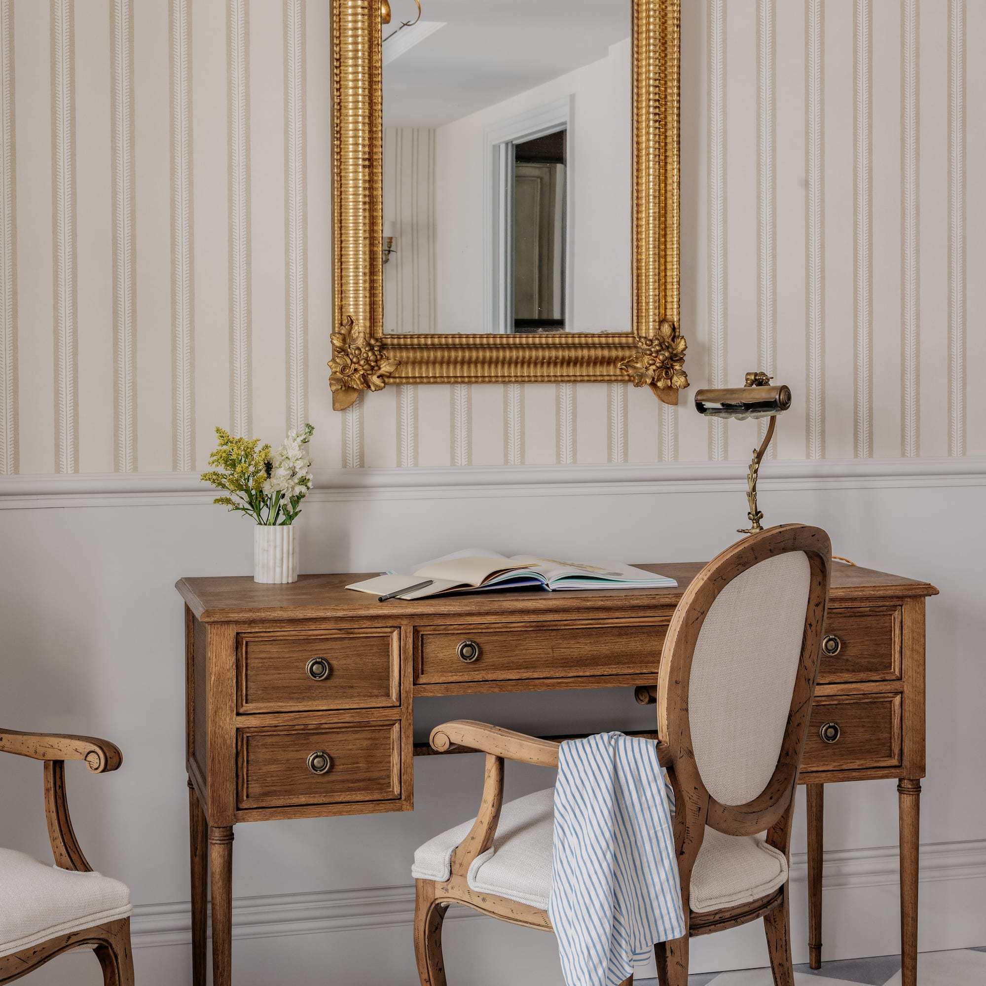 Classic wooden desk, gold mirror, striped wallpaper, checkered floor.