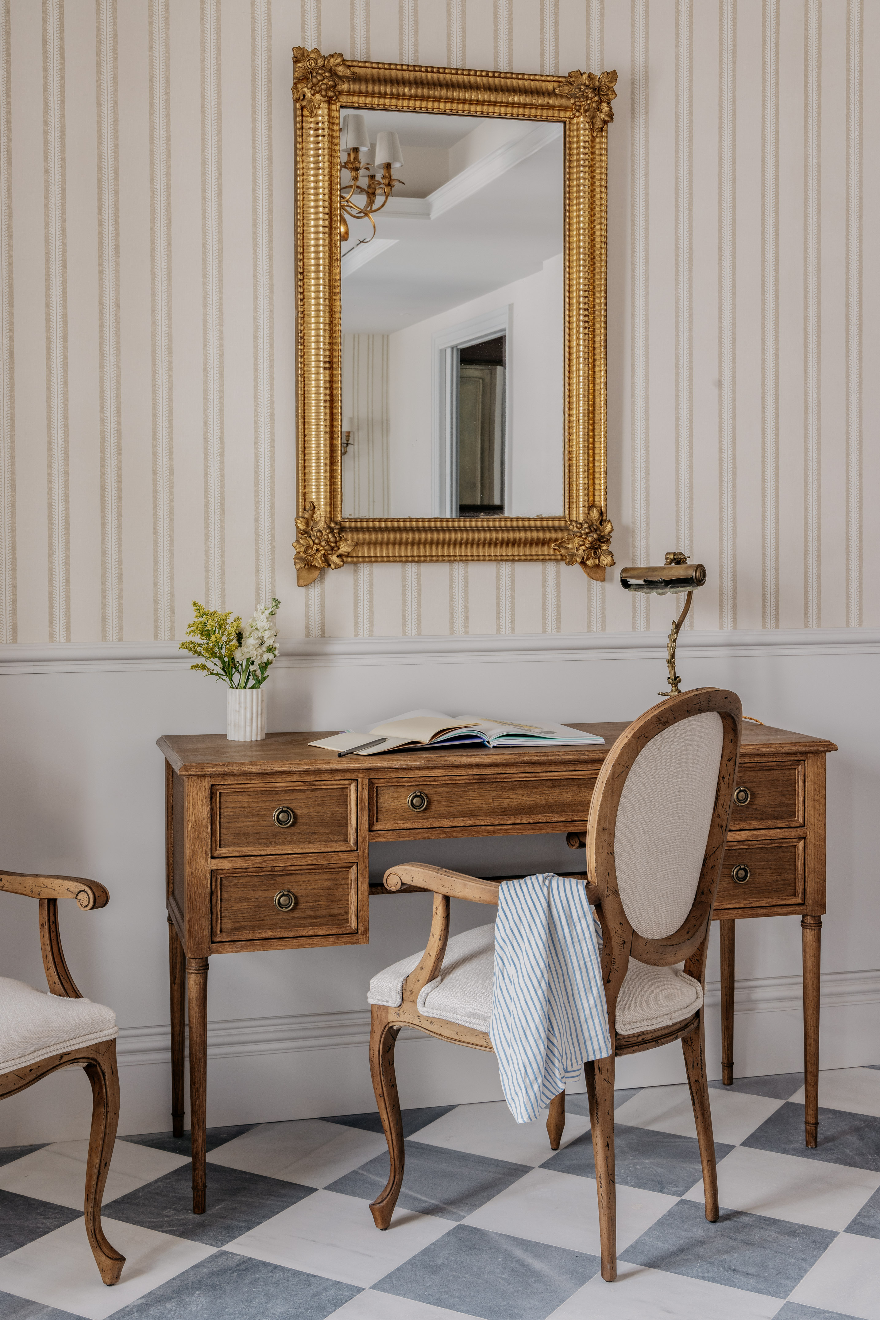 Classic wooden desk, gold mirror, striped wallpaper, checkered floor.