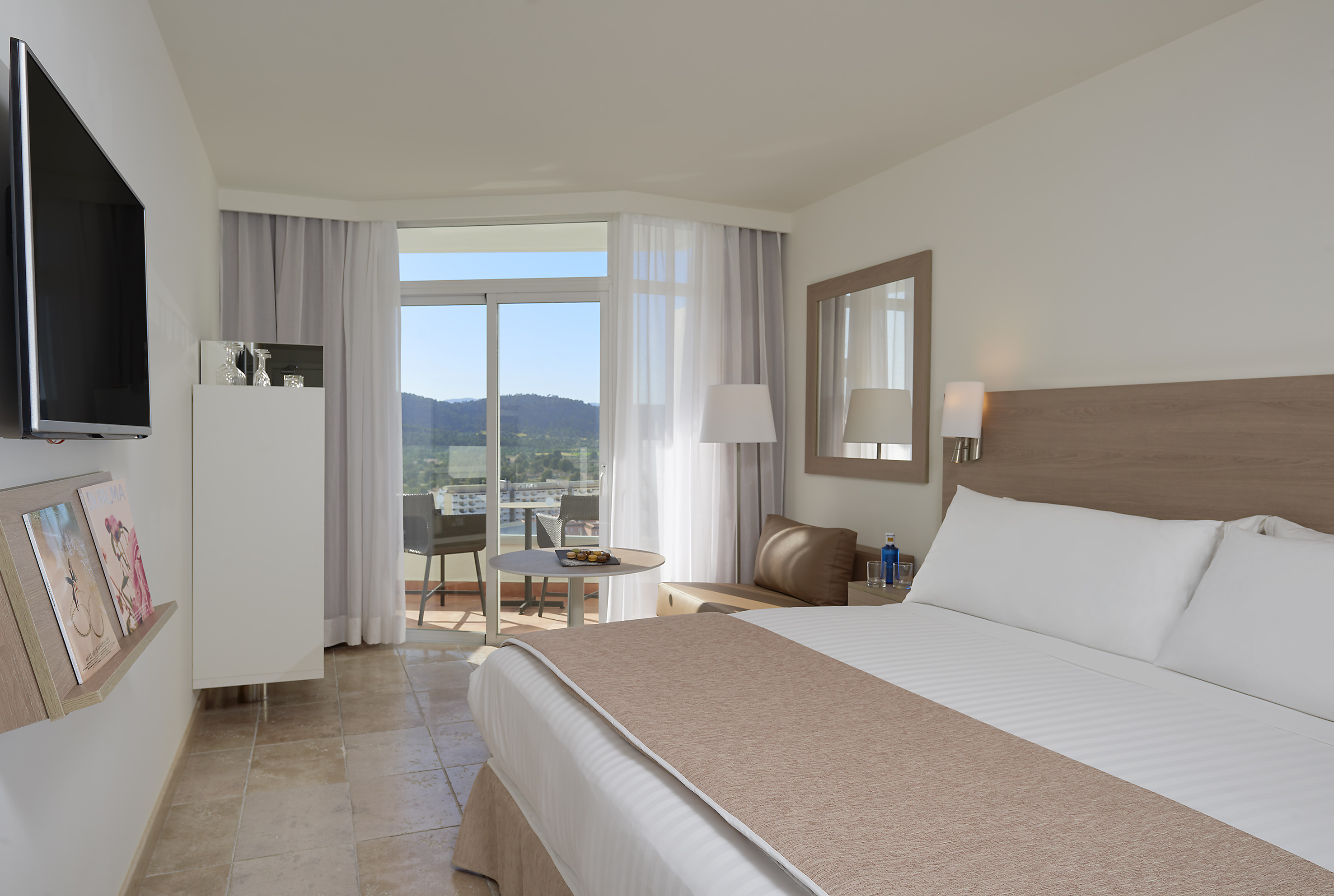 Hotel room with balcony overlooking mountains, large bed, and flat-screen TV.