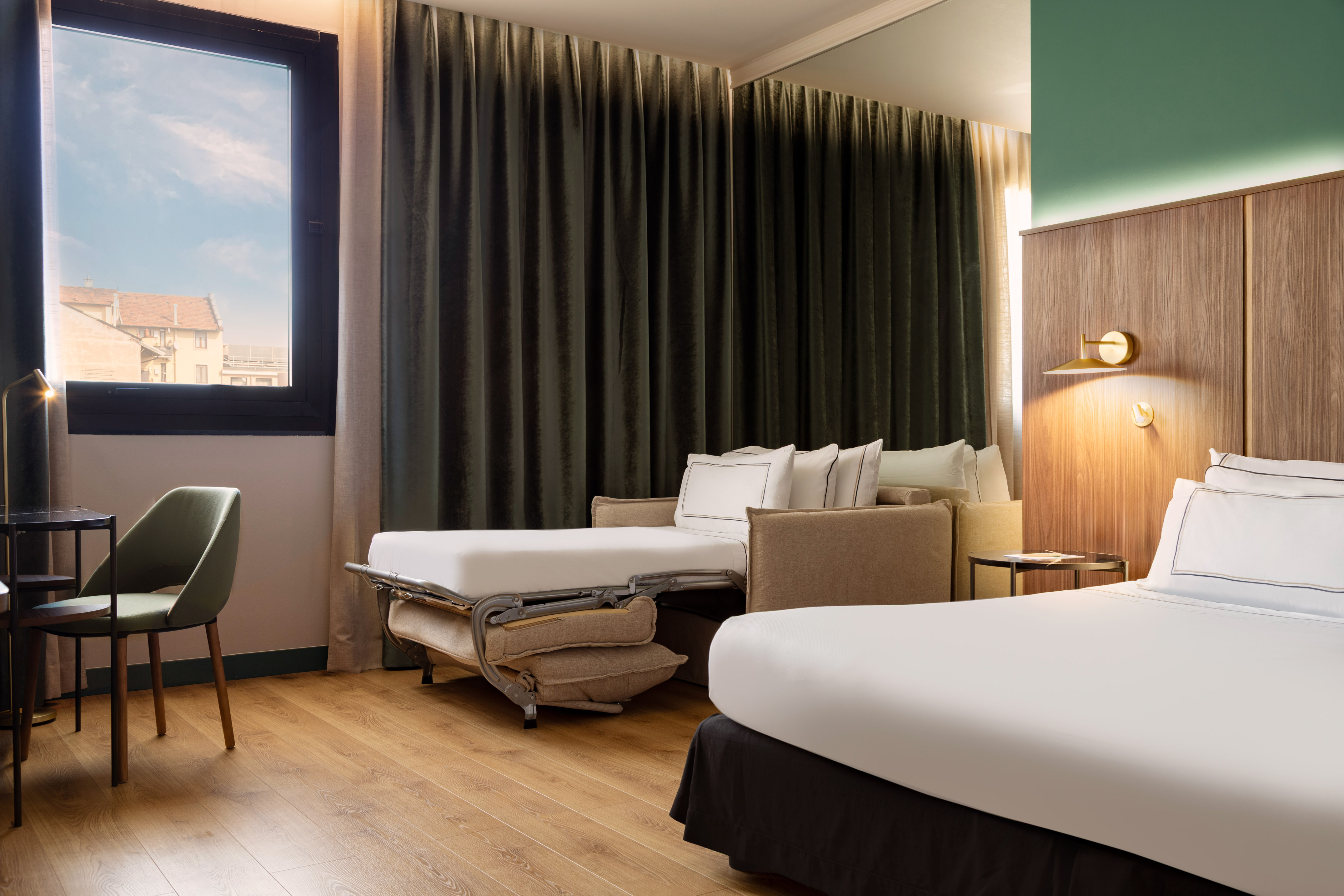 Modern hotel room with convertible sofa bed, wooden floor, and window view.