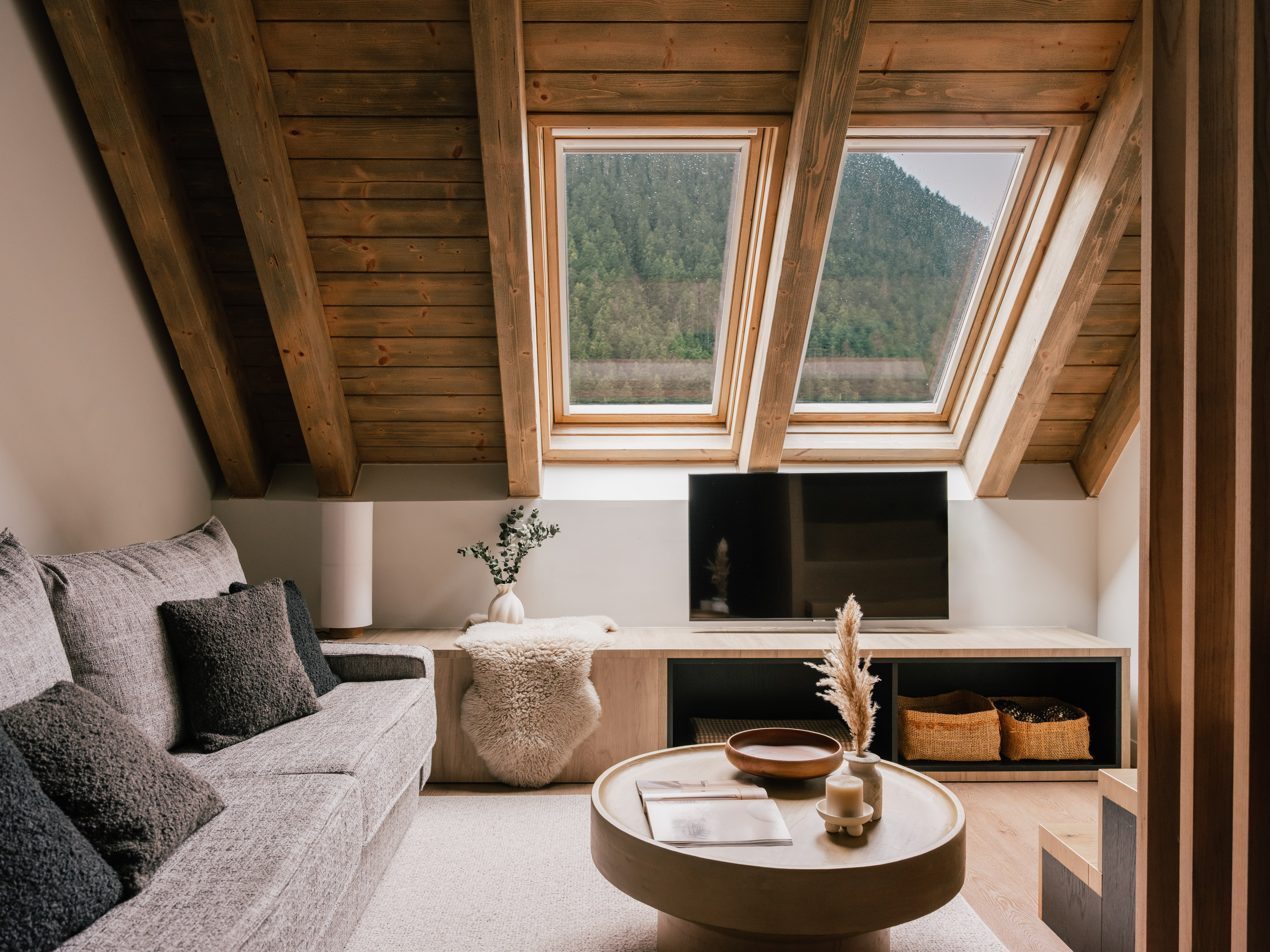 Cozy attic living room with skylight mountain view, wooden beams, and grey sofa.