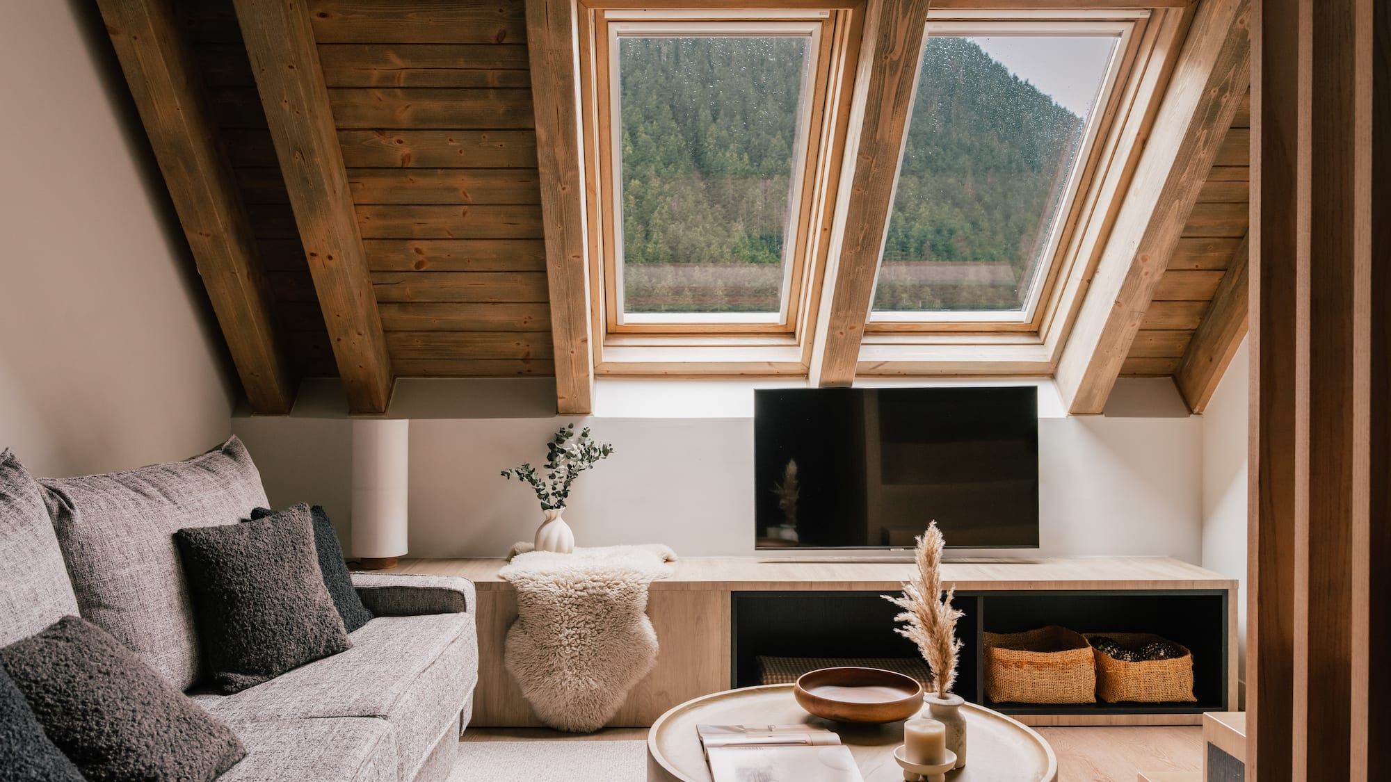Cozy attic living room with skylight mountain view, wooden beams, and grey sofa.