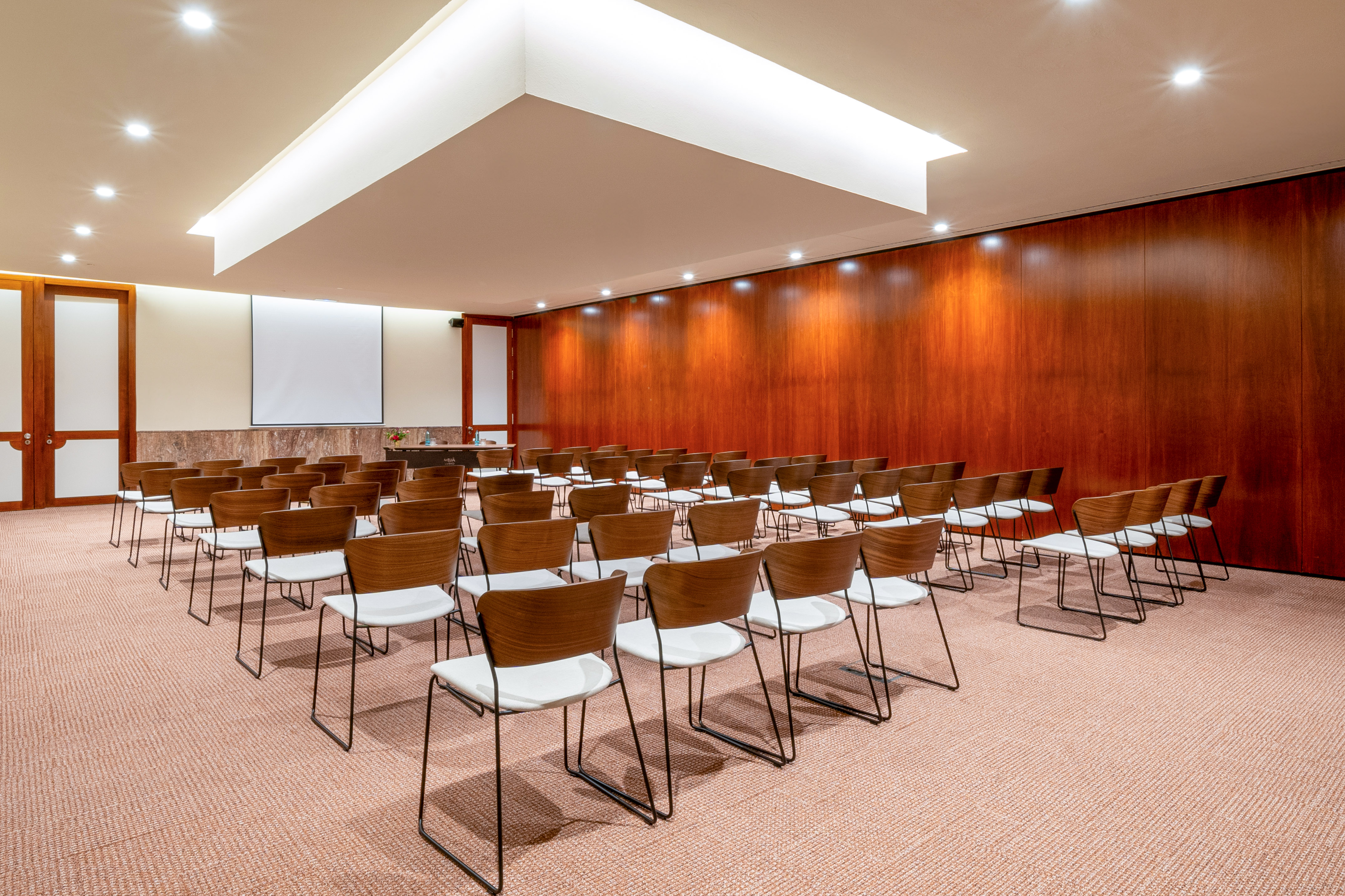Hotel meeting room with projector screen, modern chairs, and wood paneling.