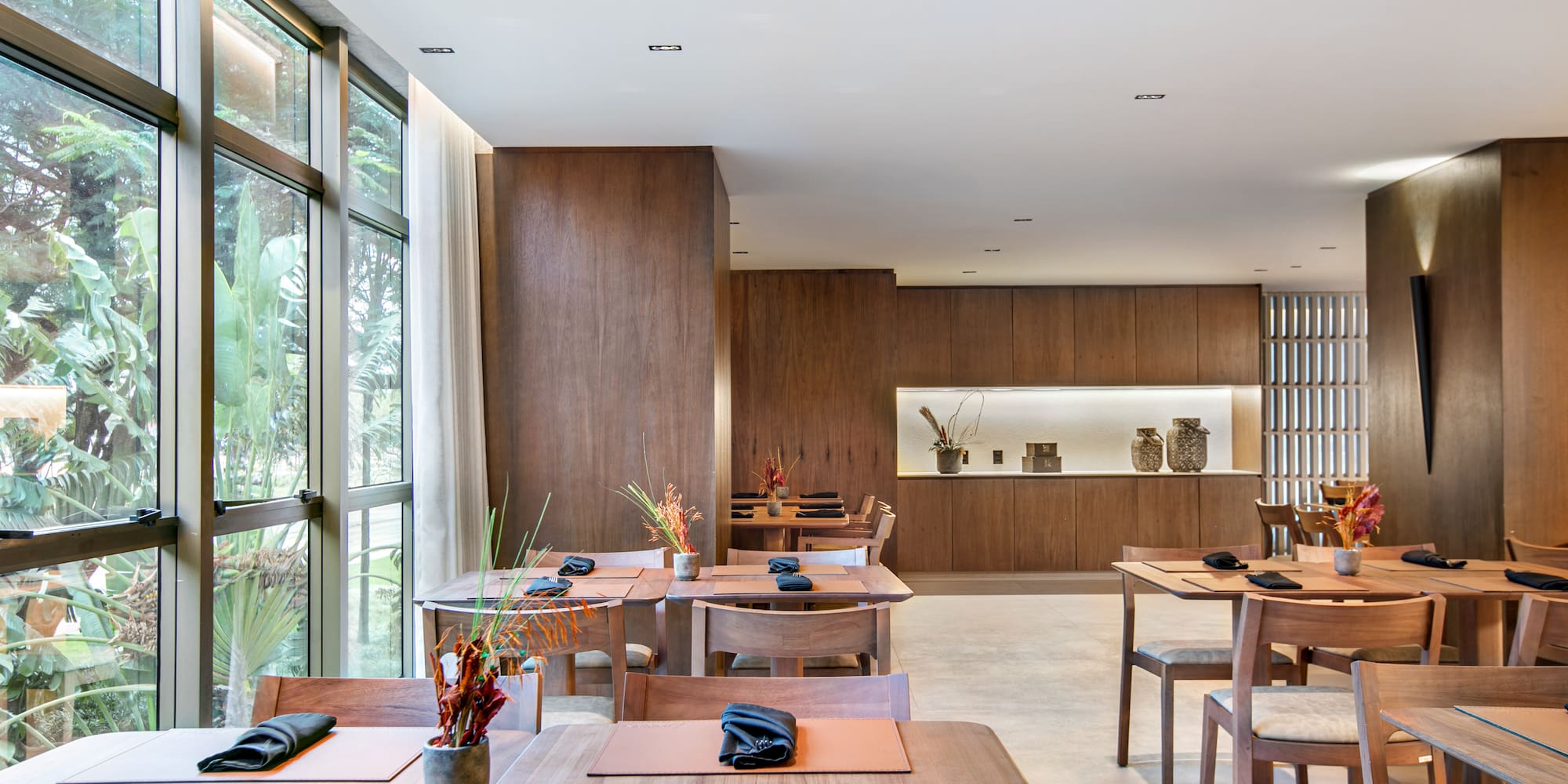 Modern restaurant with wooden tables, large windows, and a lush tropical view.