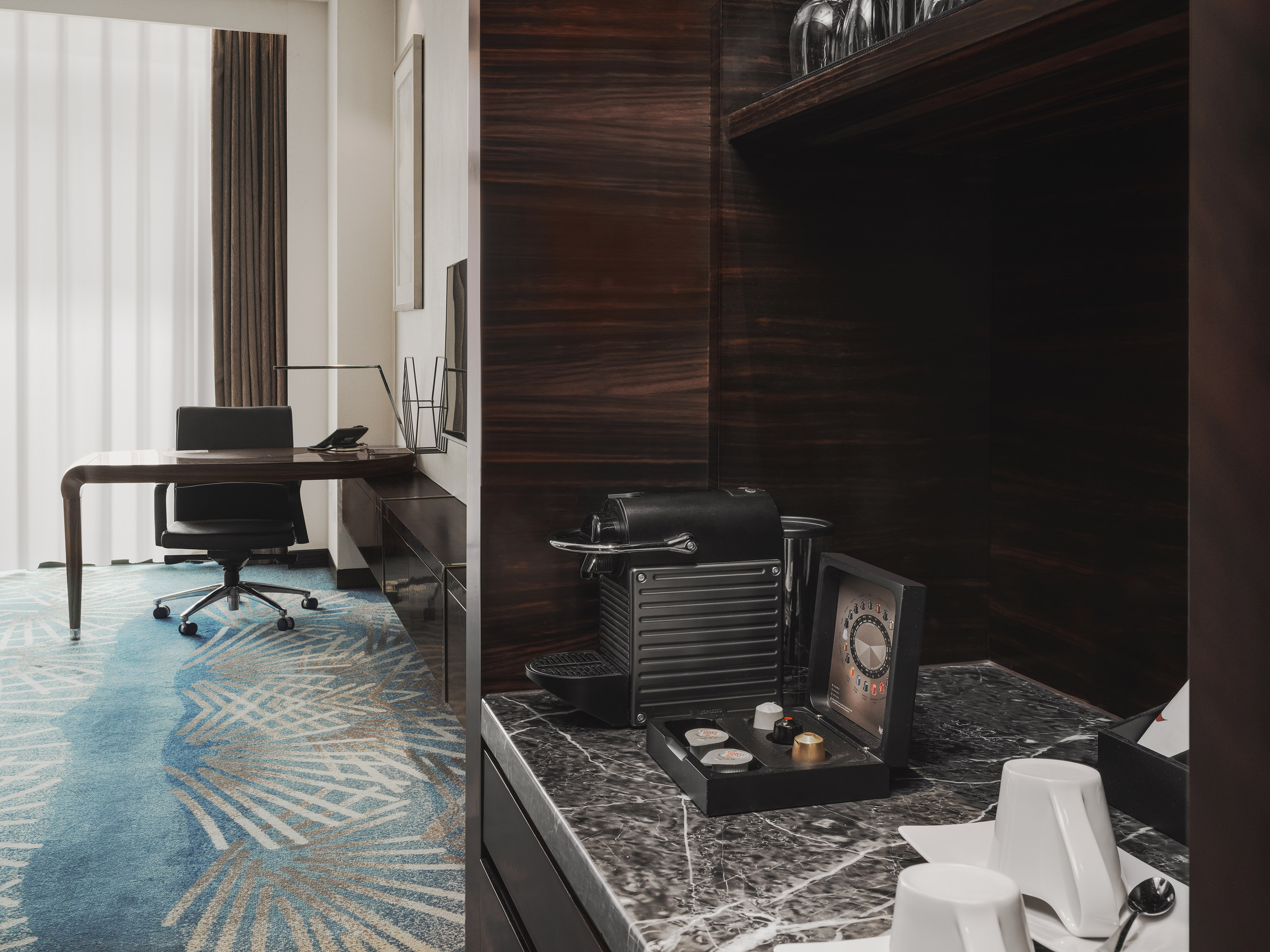 Modern hotel room: Nespresso coffee station, workspace, and patterned blue carpet.