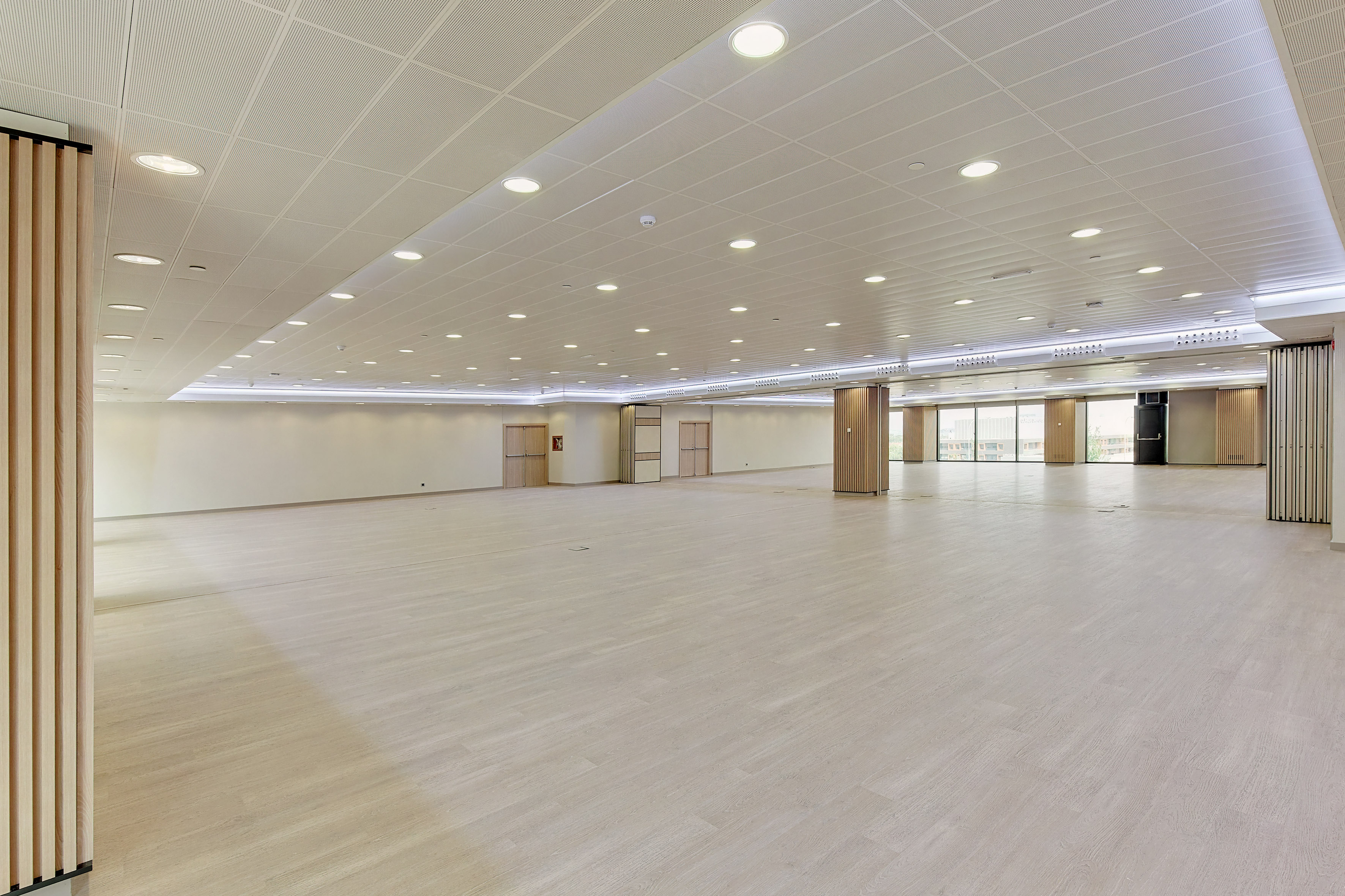 Empty modern event hall with light wood floor and recessed lighting.