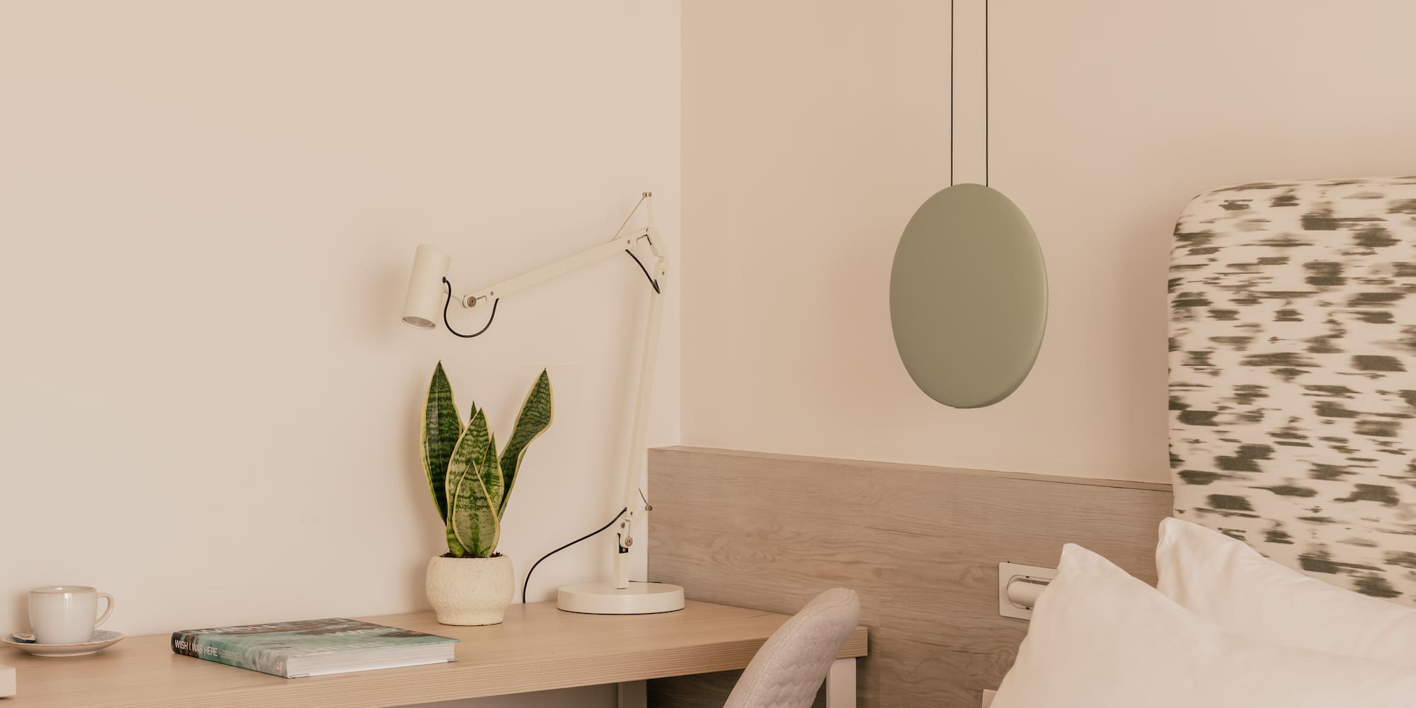 Modern bedroom with workspace, snake plant, bed, and minimalist decor.