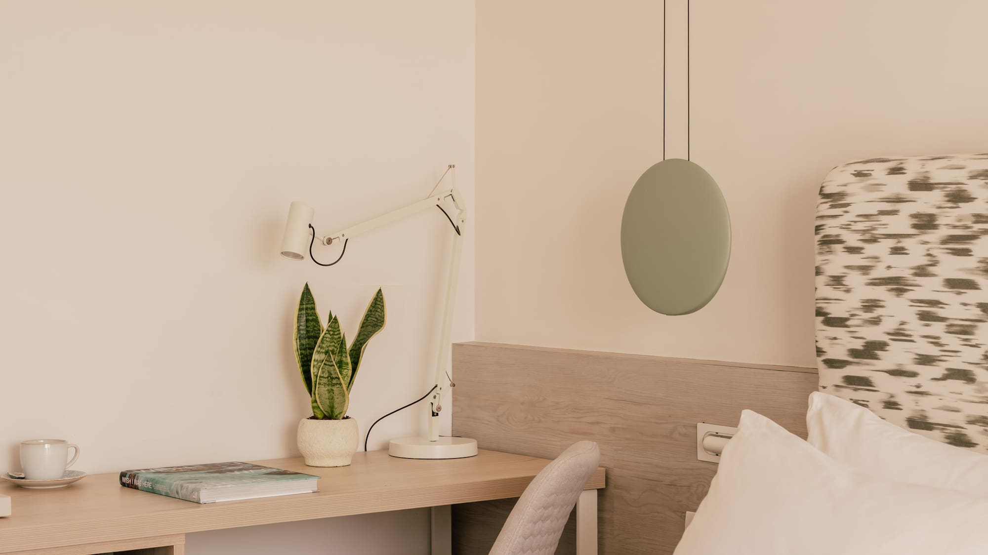 Modern bedroom with workspace, snake plant, bed, and minimalist decor.