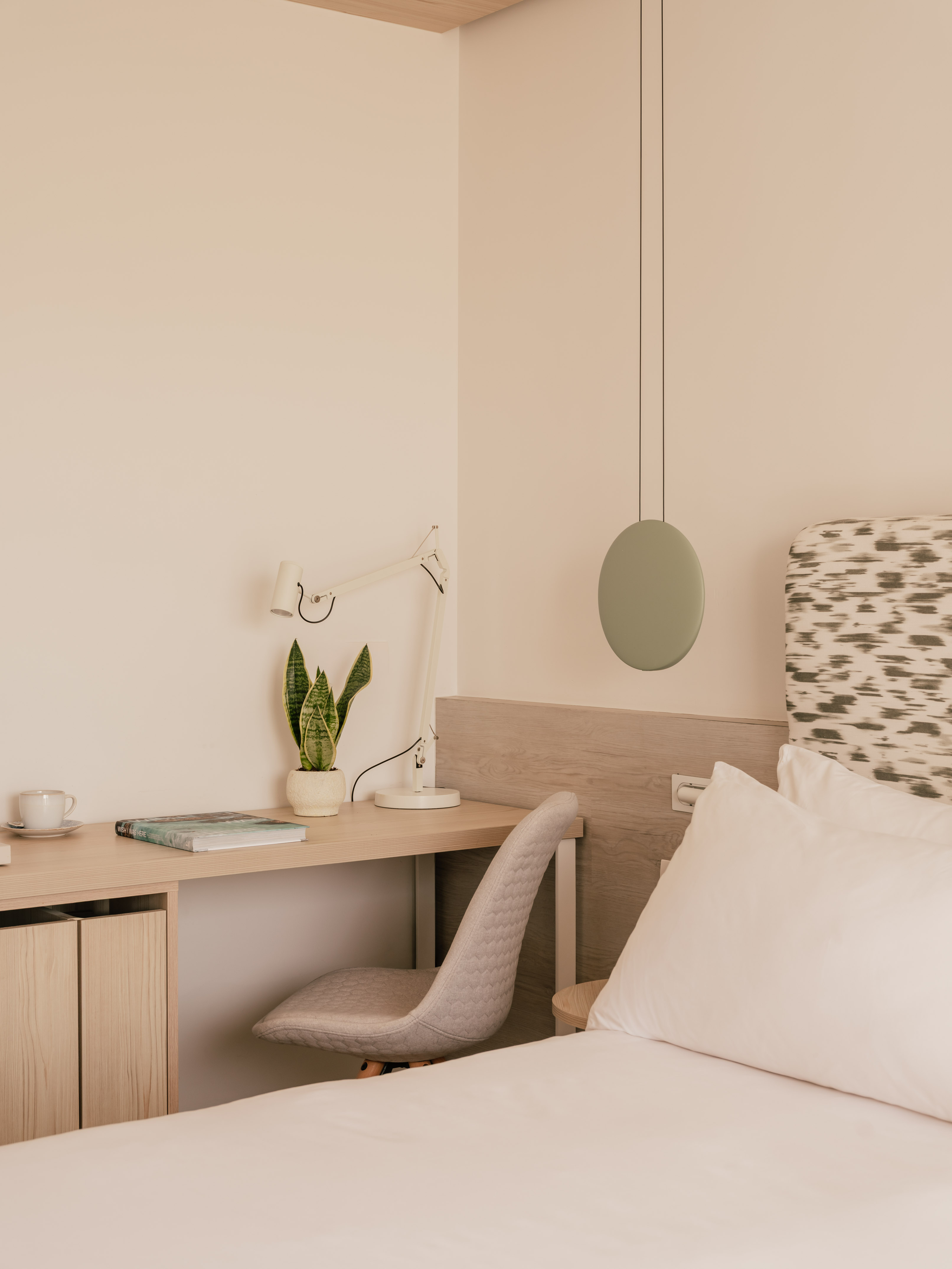 Modern bedroom with workspace, snake plant, bed, and minimalist decor.