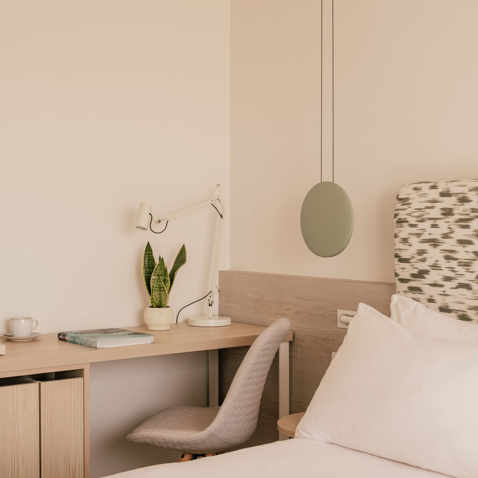 Modern bedroom with workspace, snake plant, bed, and minimalist decor.