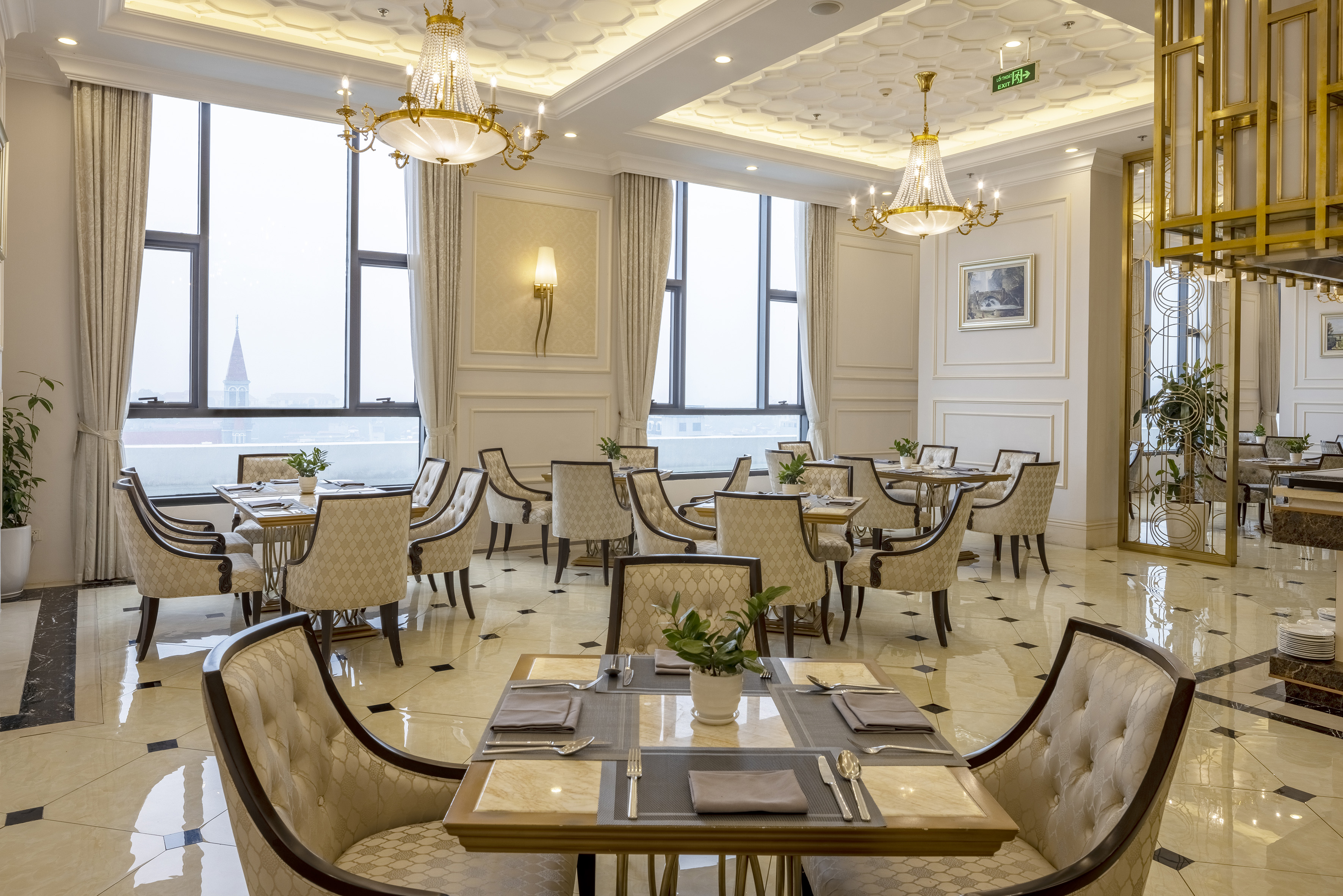 Elegant dining room with set tables, plush chairs, chandeliers, and city view.